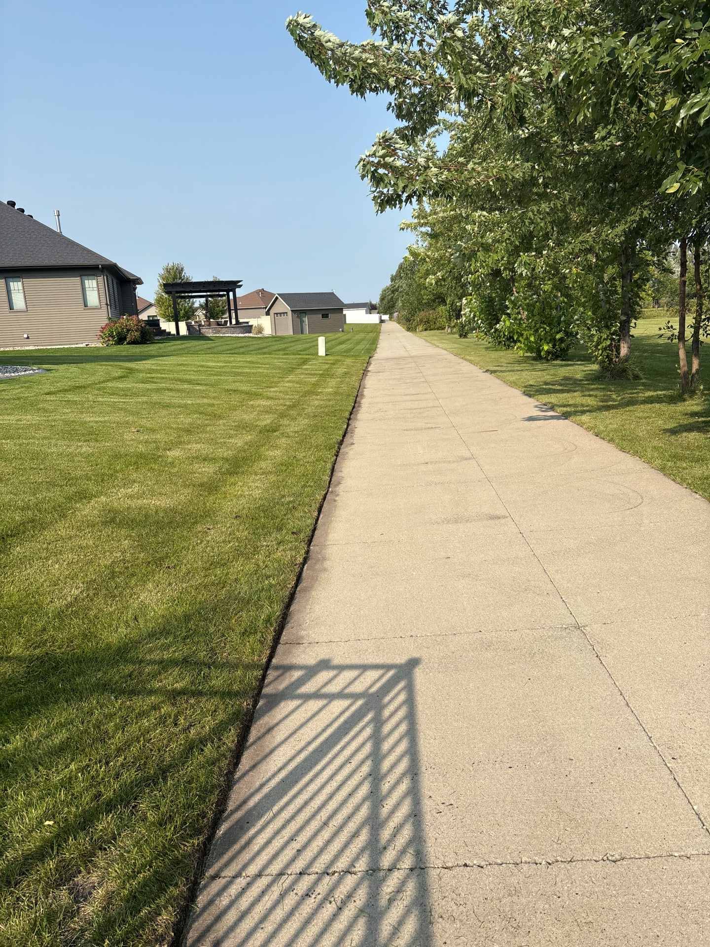 A paved sidewalk extends into the distance, bordered by a mowed lawn and trees, with houses visible in the background.