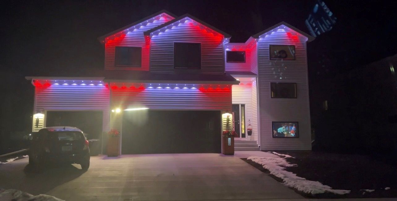 A two-story suburban house at night, decorated with red, white, and blue exterior lights, with a car parked in the driveway.