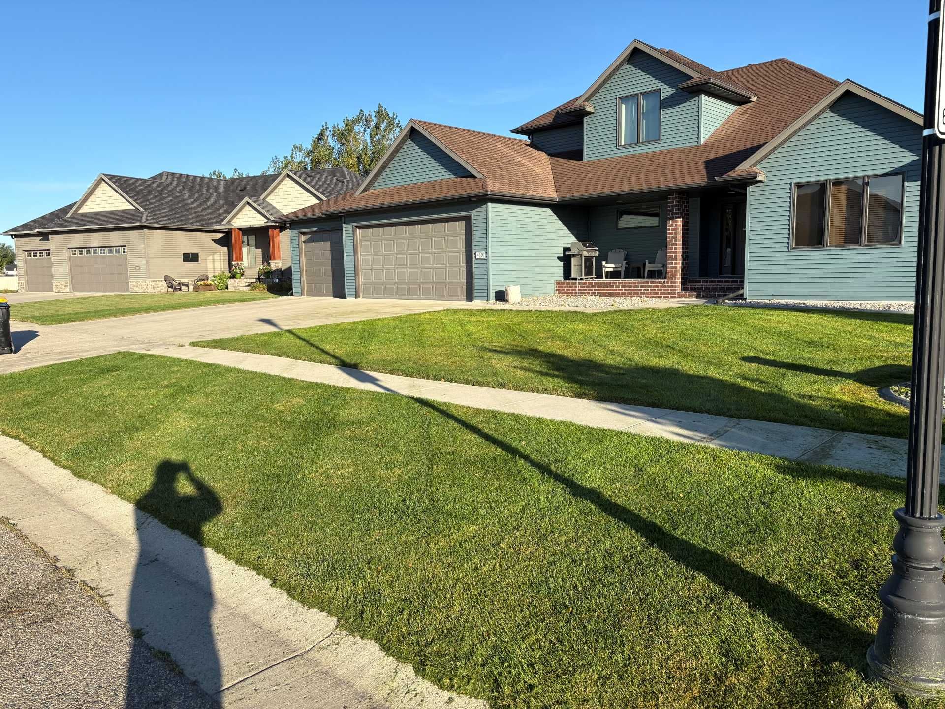 A wide shot of two suburban houses with garages and green lawns, with a person's shadow cast in the foreground.