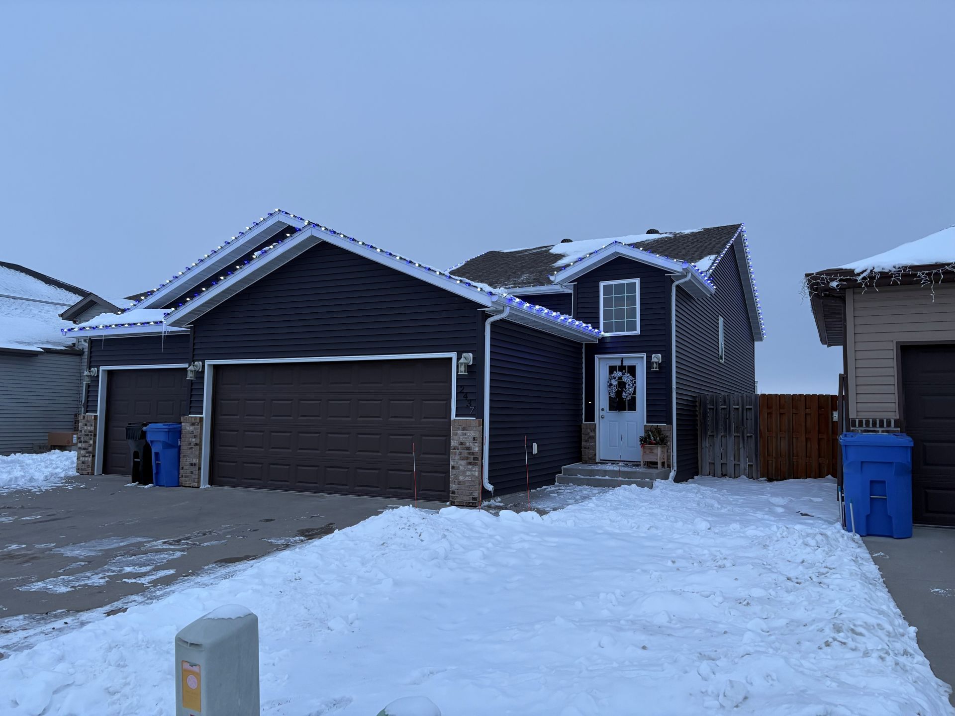 A dark blue house with a two-car garage, stone accents, and a white front door, surrounded by snow in winter.