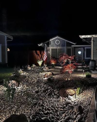 A landscaped front yard at night with rock ground cover, illuminated by pathway lights leading to a small house.