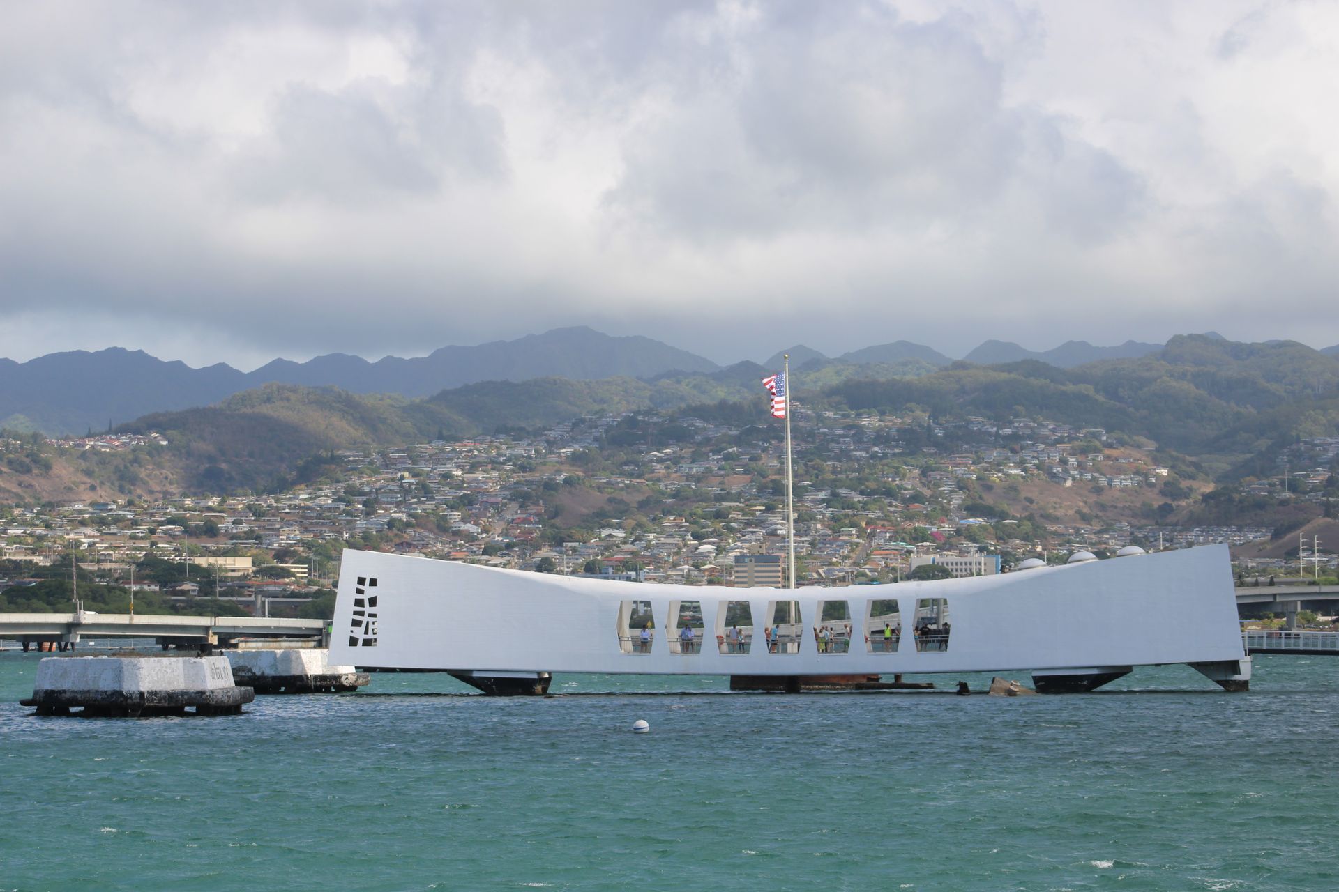 White USS Arizona Memorial over turquoise water, mountains in background.