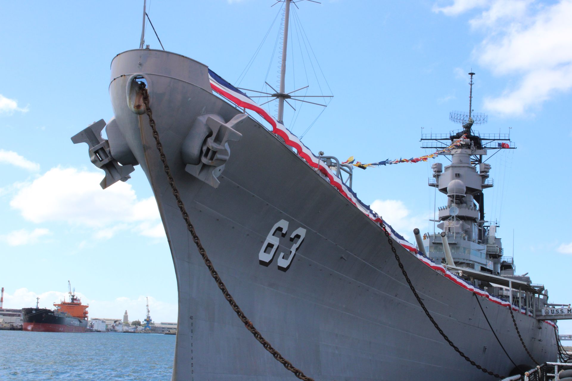 Battleship USS Missouri (BB-63) at a pier, painted gray, with the number 63. Red, white, and blue decorations.