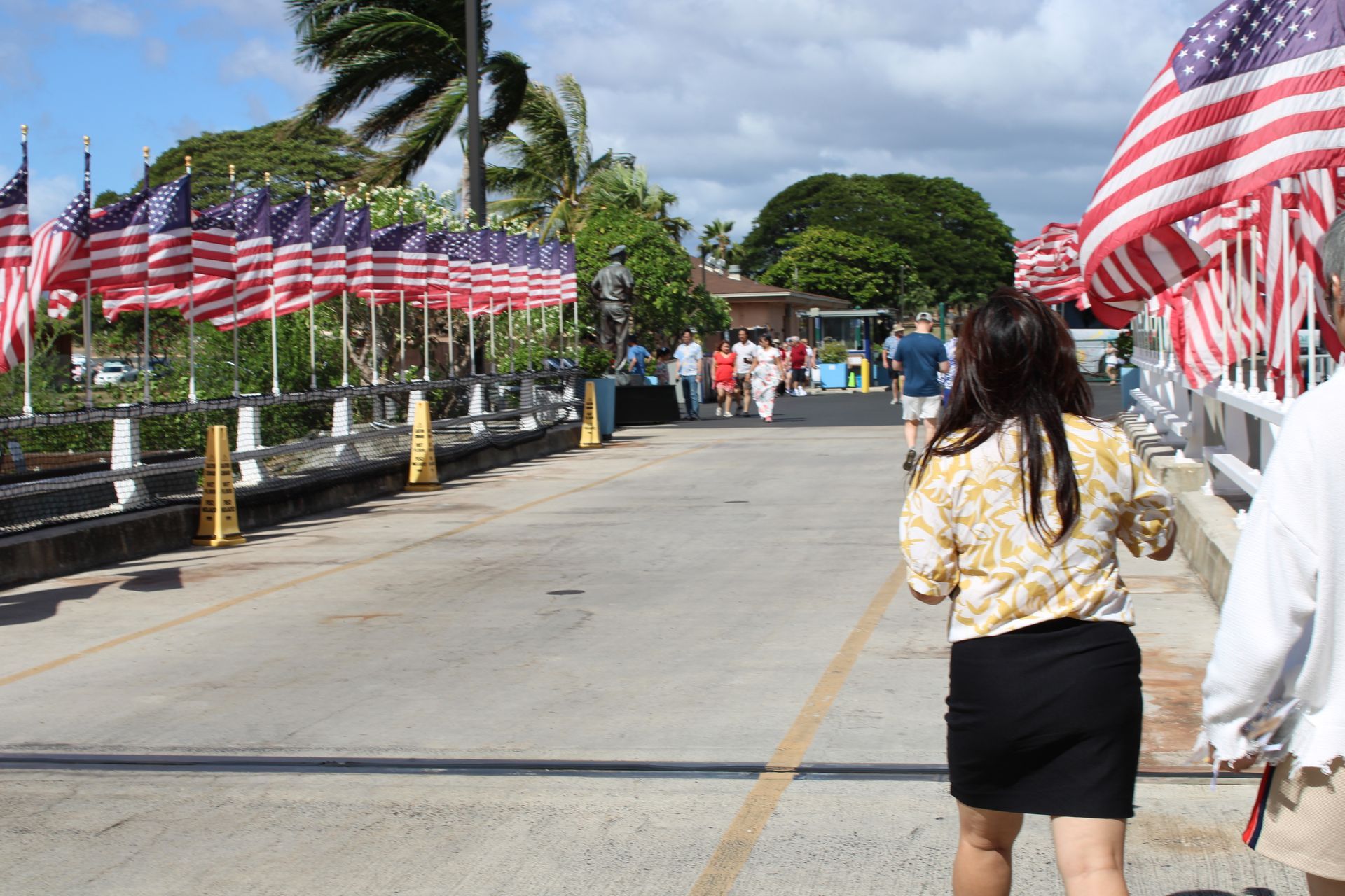 Bridge lined with American flags; people walking toward a building on a sunny day.