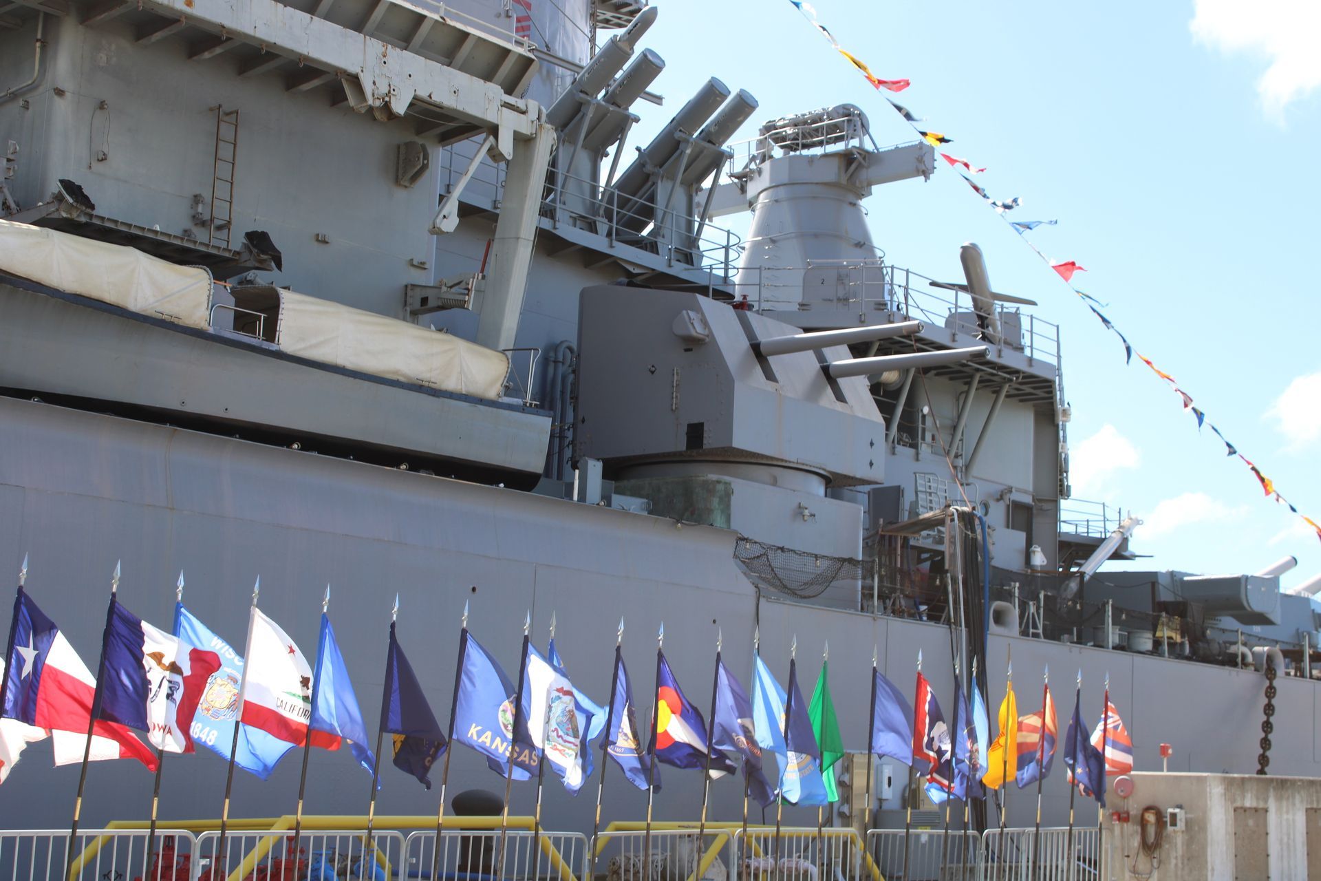 Large gray battleship docked, with colorful flags displayed.