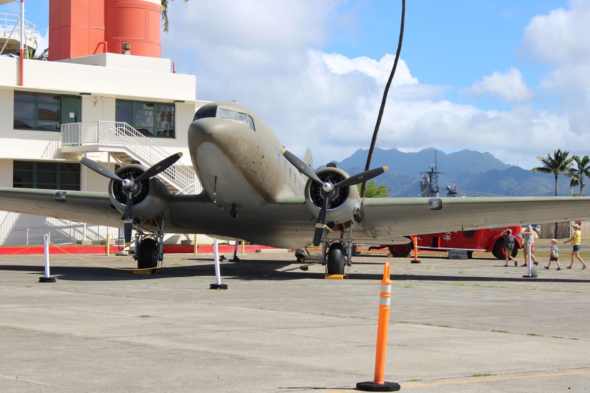 Man posing with a statue at Polynesian Cultural Center in Hawaii. Wearing red shorts and green shirt, arms raised.