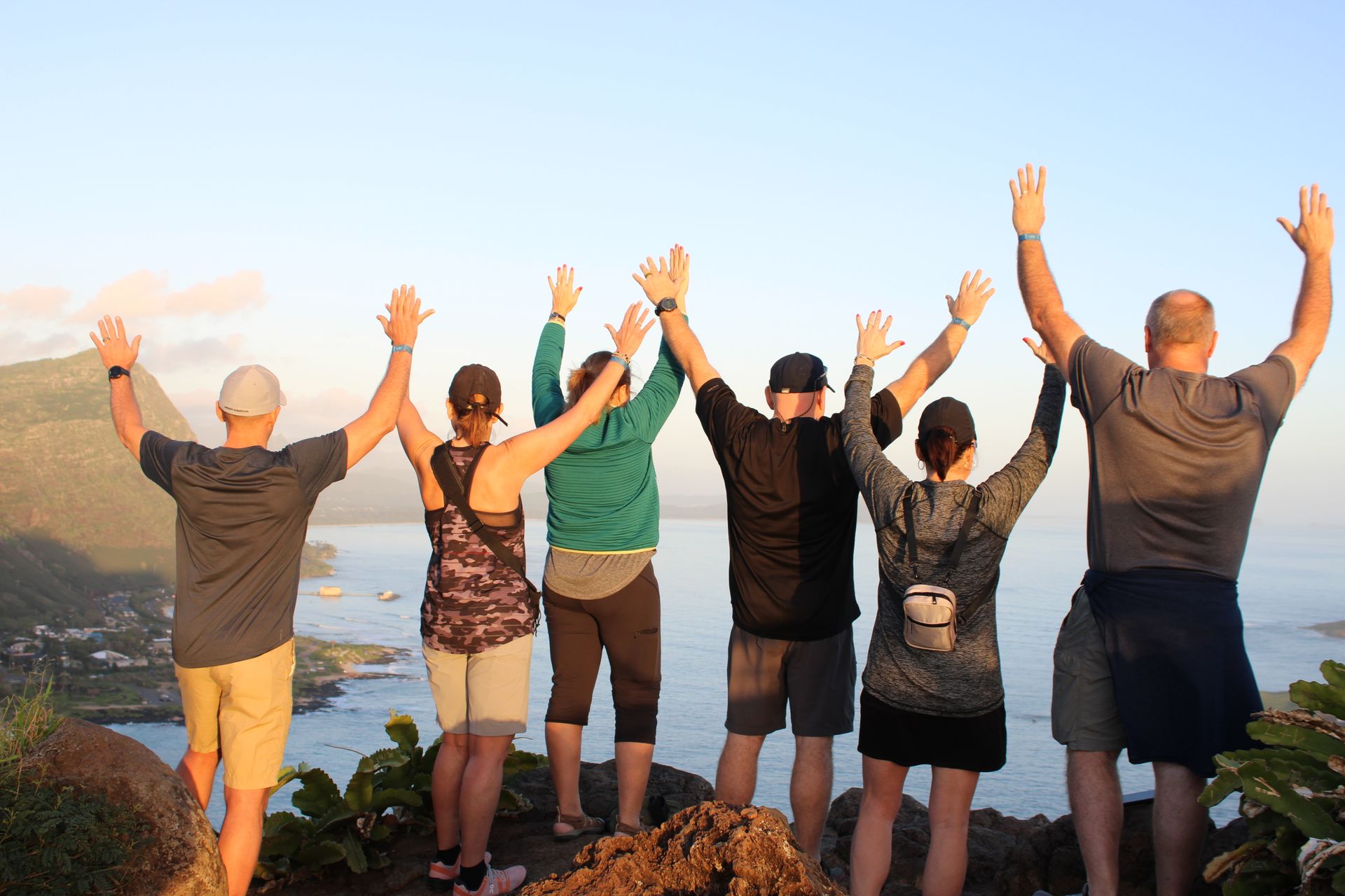 A group of people are standing on top of a hill with their arms in the air.