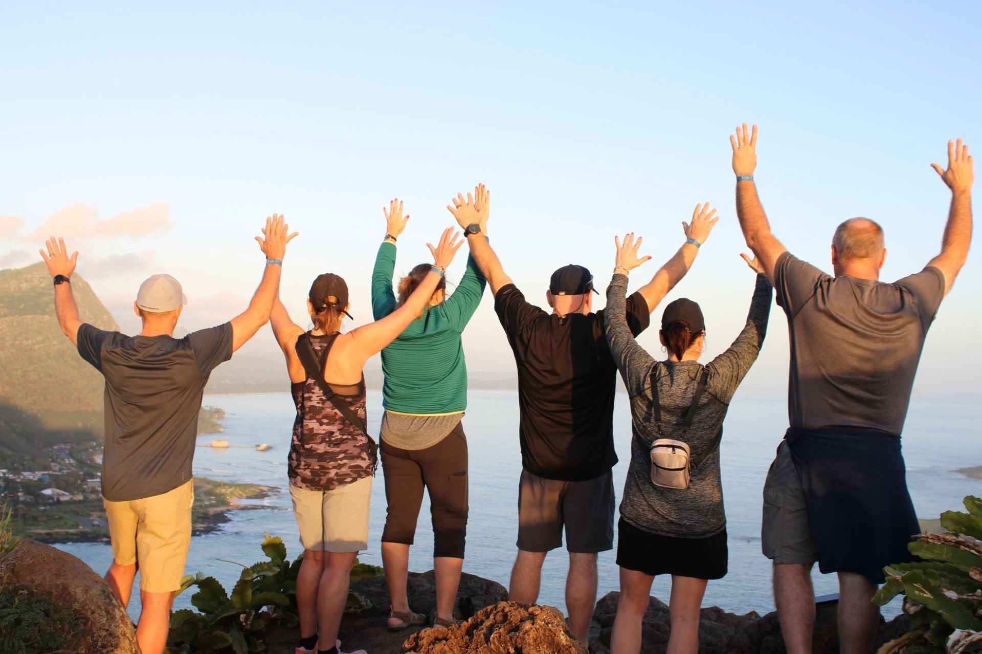 A group of people are standing on a cliff with their arms in the air.