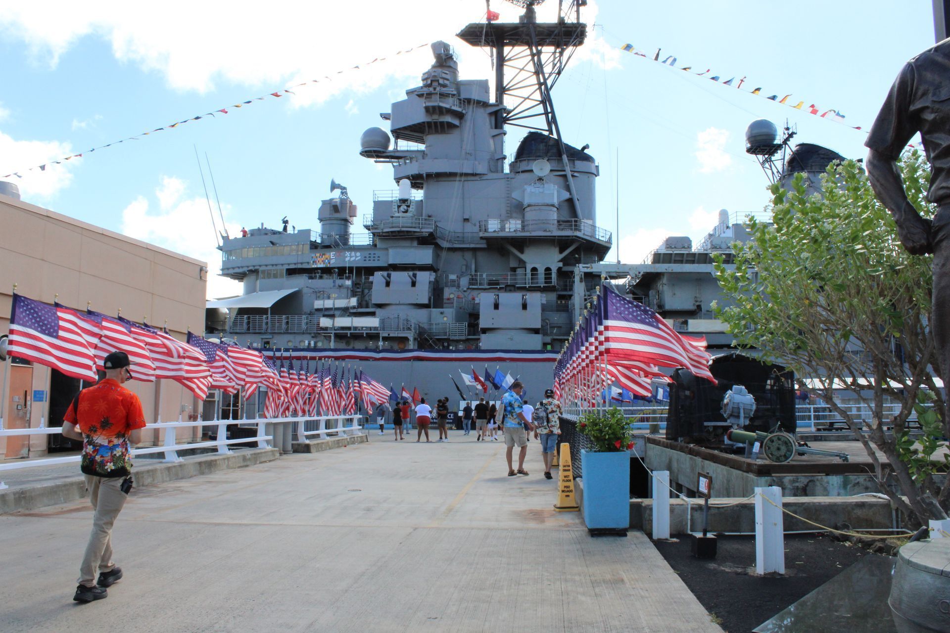 Battleship with American flags, people walking, sunny day.
