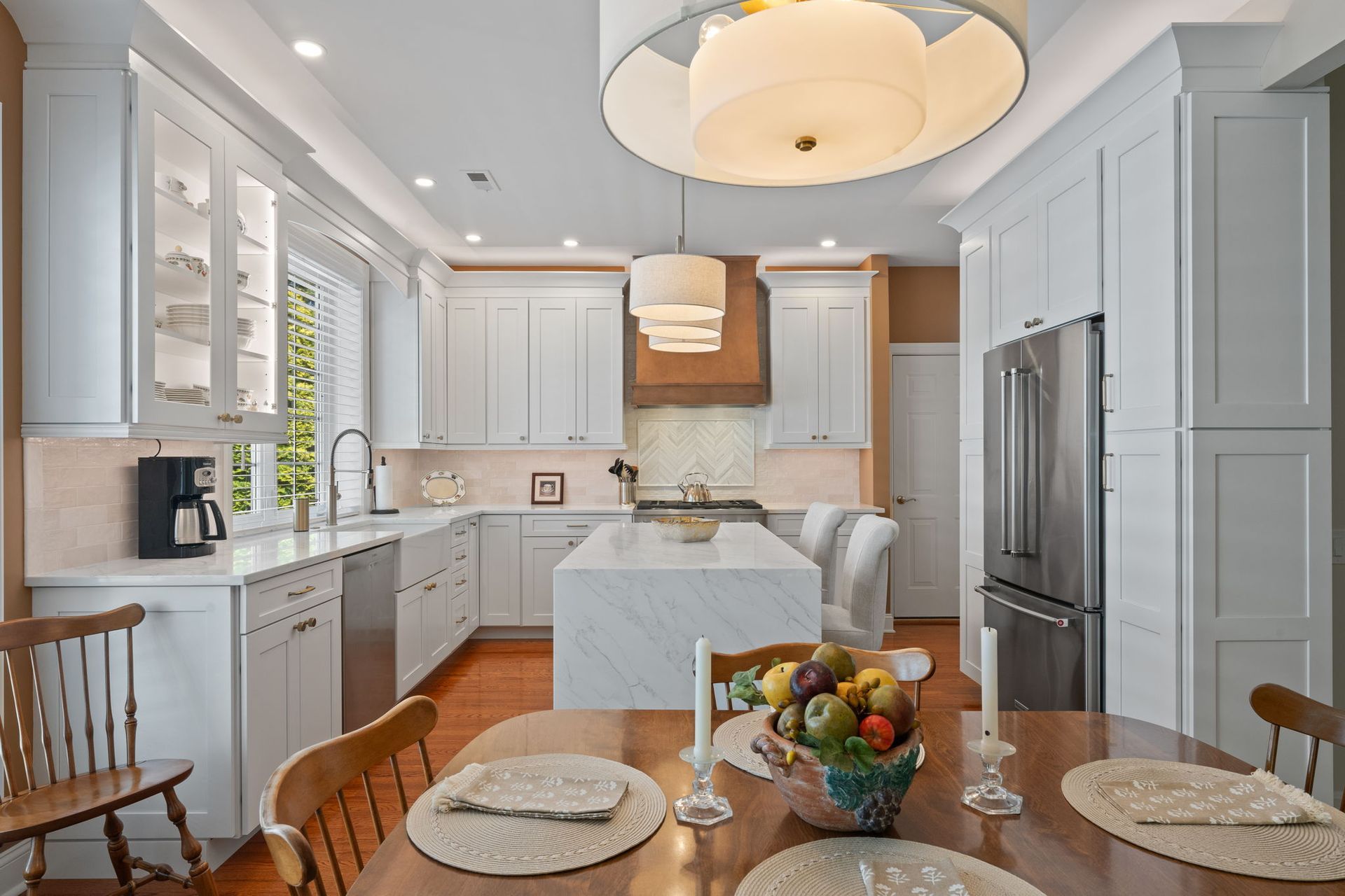 Bright white kitchen with island, stainless fridge, and wooden dining table set in foreground In Bucks County PA