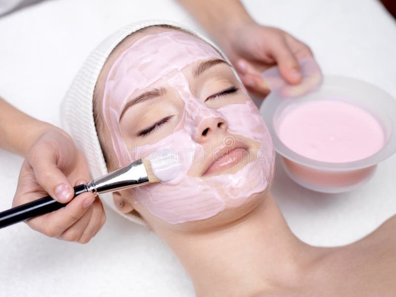 A woman is getting a pink mask on her face.