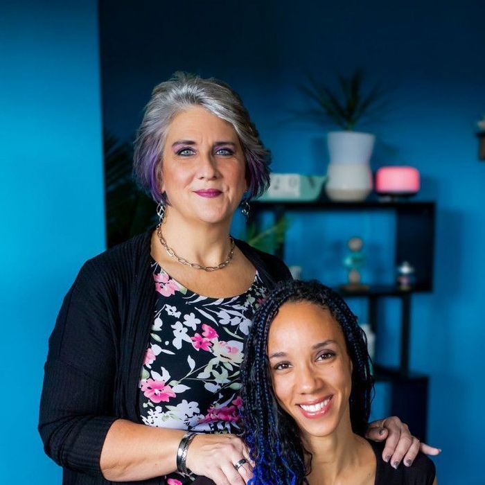 Two women are posing for a picture in front of a blue wall.