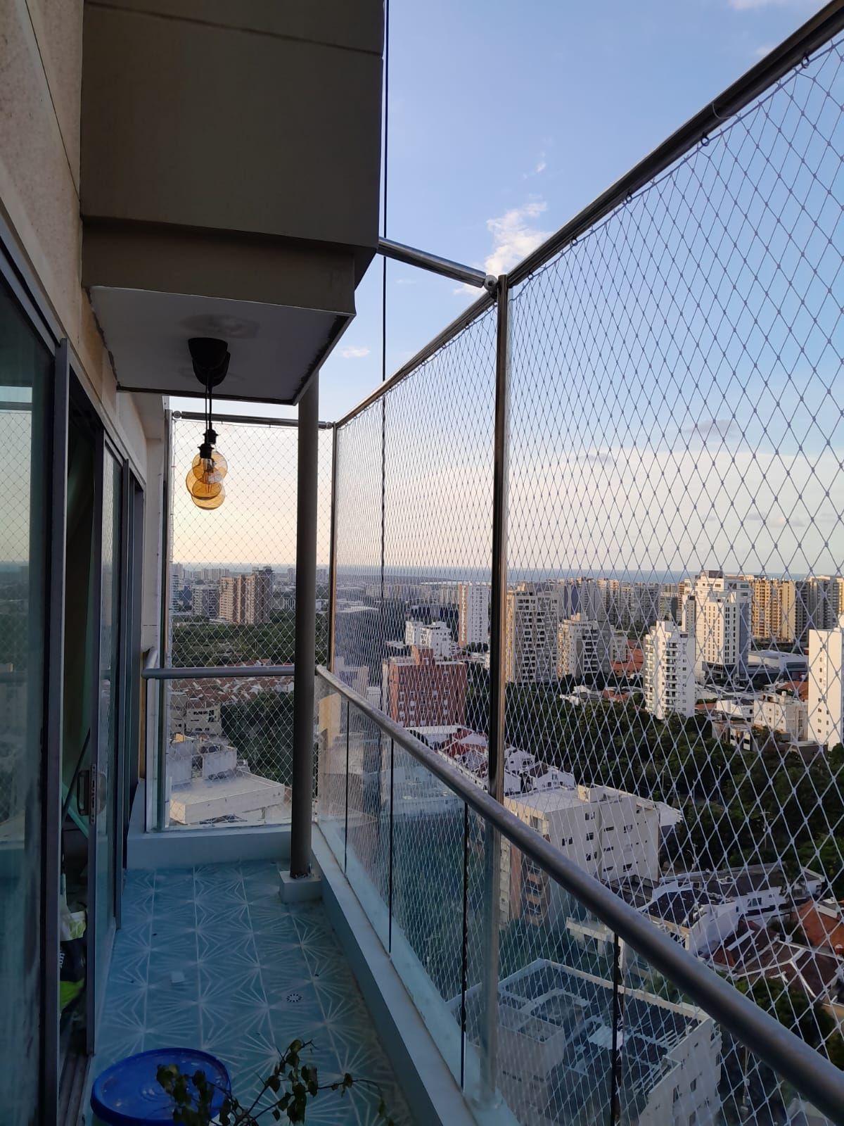 Balcón de un rascacielos con red de seguridad, con vistas a la ciudad al atardecer. Una bombilla cuelga del techo.