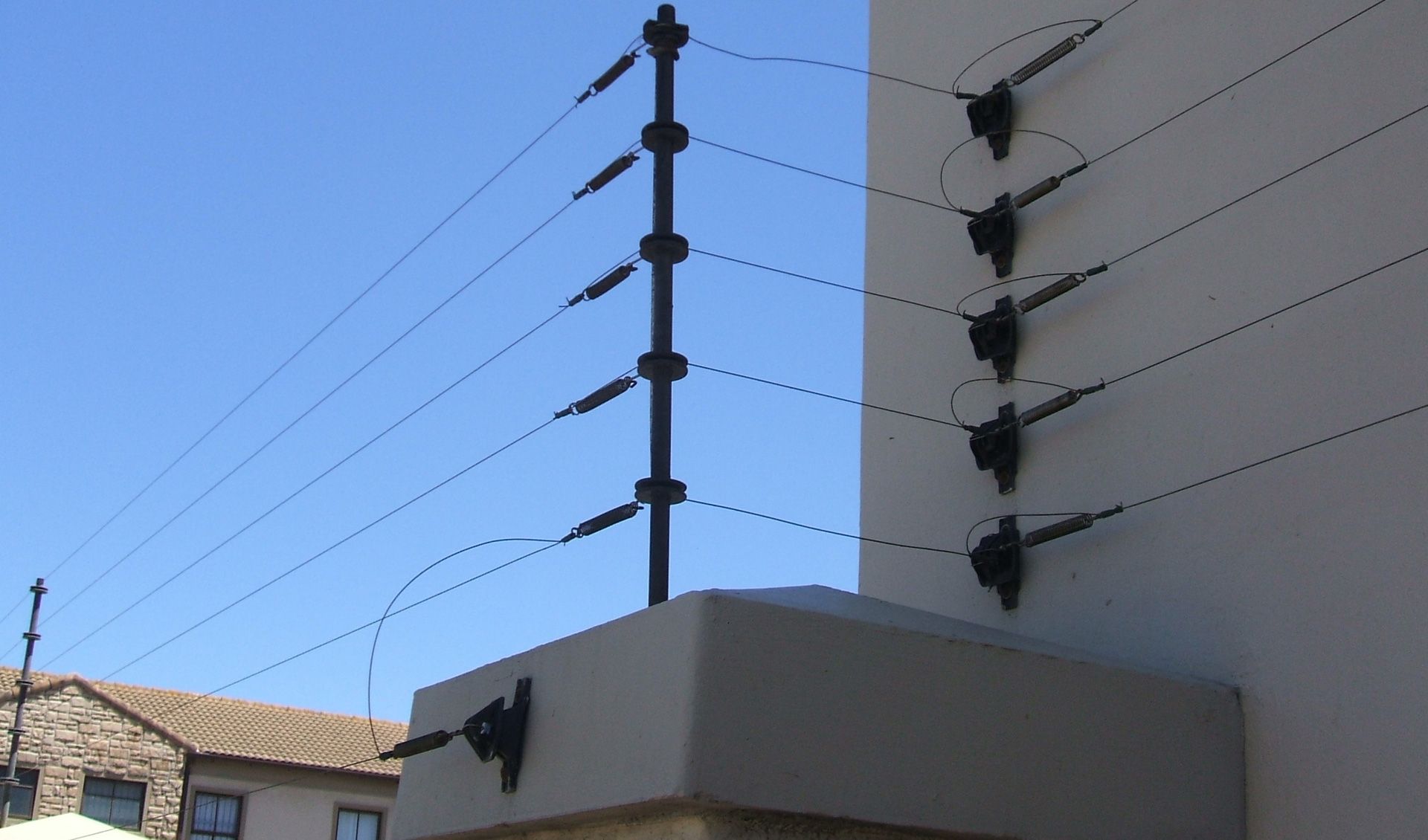 Valla electrificada sobre un muro blanco bajo un cielo azul.