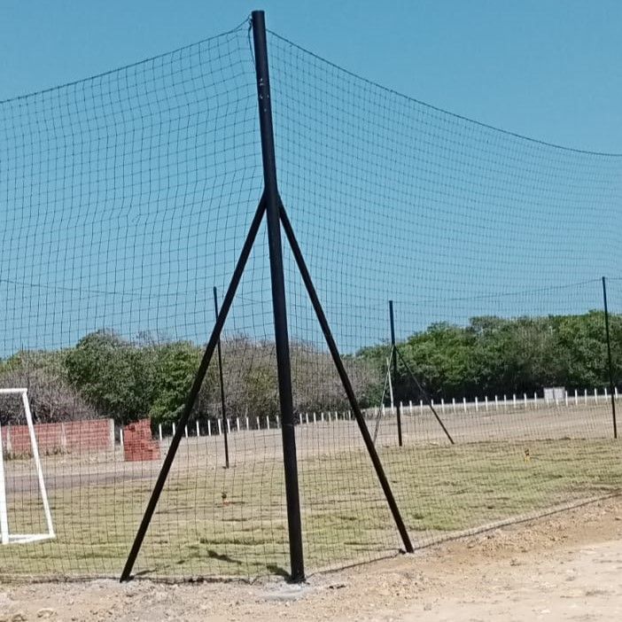 Una valla de malla negra sostenida por postes y puntales negros se alza sobre un campo de hierba, bajo un cielo azul.