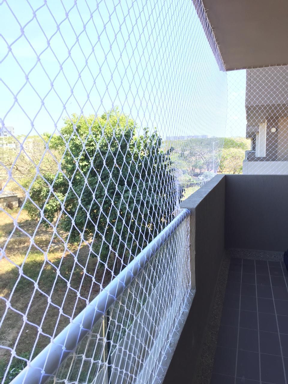 Red de seguridad blanca en un balcón, que protege la vista de los árboles y los edificios.