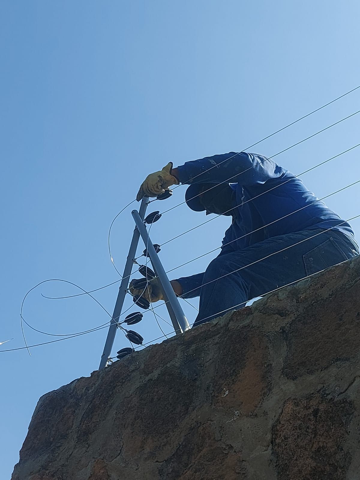 Valla electrificada sobre un muro blanco bajo un cielo azul.