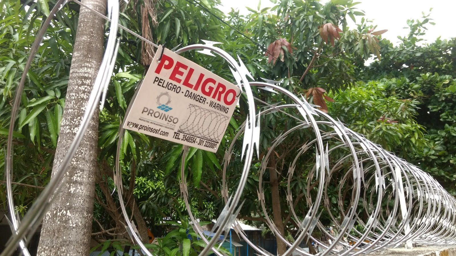 Bobinas de alambre de púas sobre una puerta y un muro metálicos, presumiblemente por motivos de seguridad en un entorno urbano.