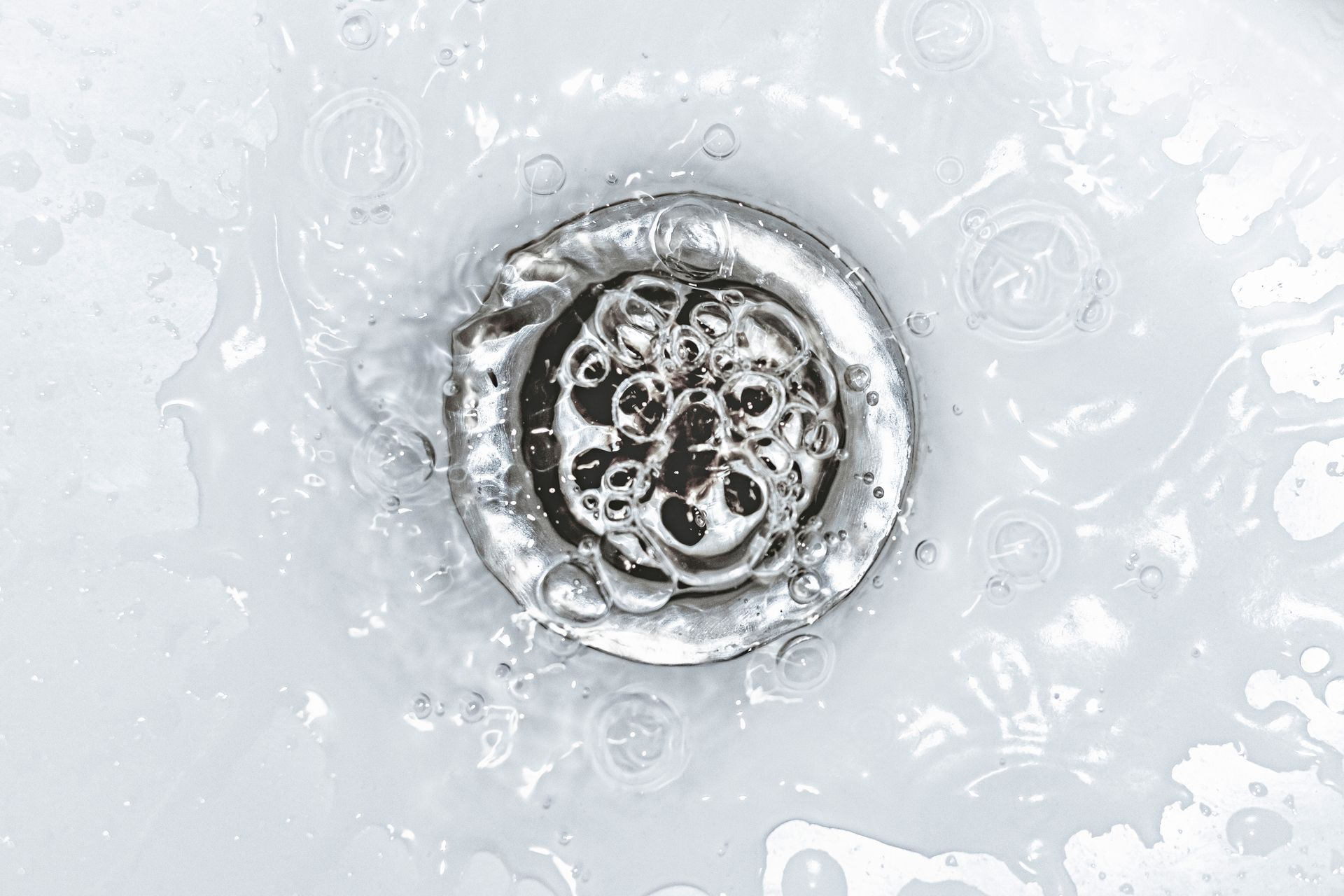 Hand using a drain snake to unclog a white bathroom sink.