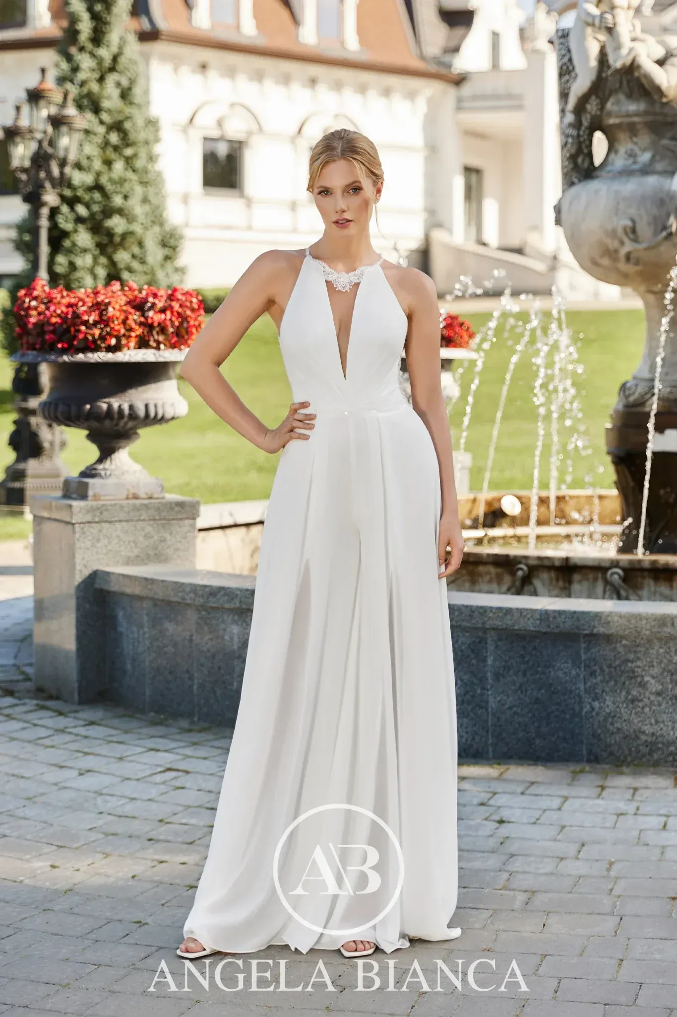 Woman in a white wedding dress with long, lacy sleeves stands on a wooden dock near a lake.