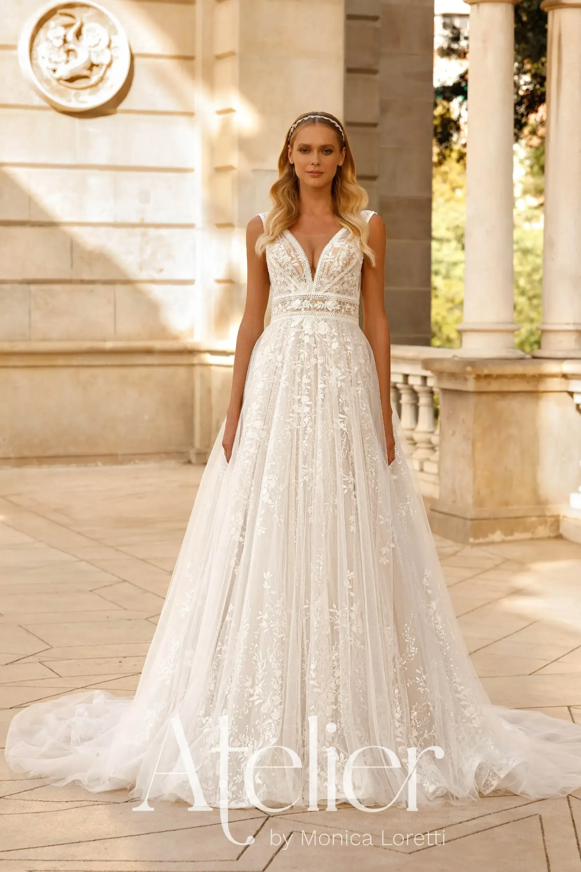 Woman in white halter gown, posed in front of a fountain and ornate building. She has blonde hair, and is smiling.