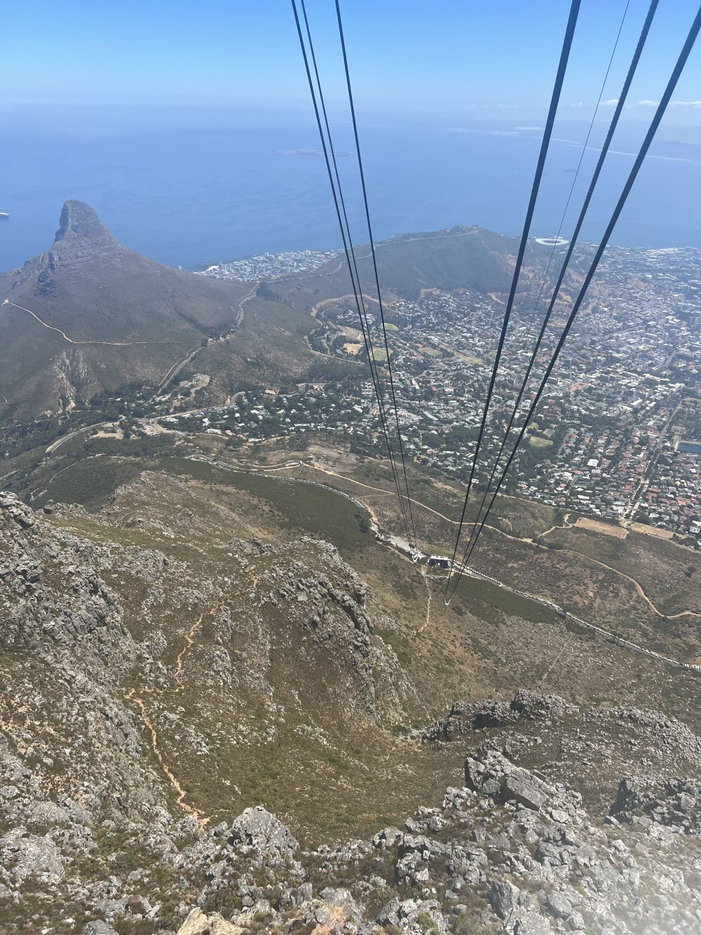 View from a cable car descending Table Mountain, Cape Town, South Africa, overlooking a city and the ocean.