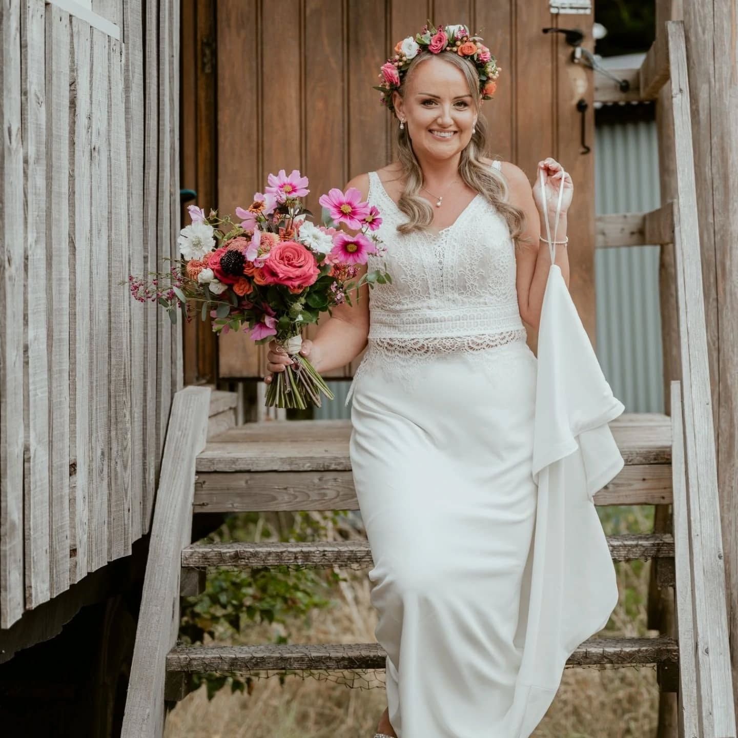 Woman in white halter gown, posed in front of a fountain and ornate building. She has blonde hair, and is smiling.