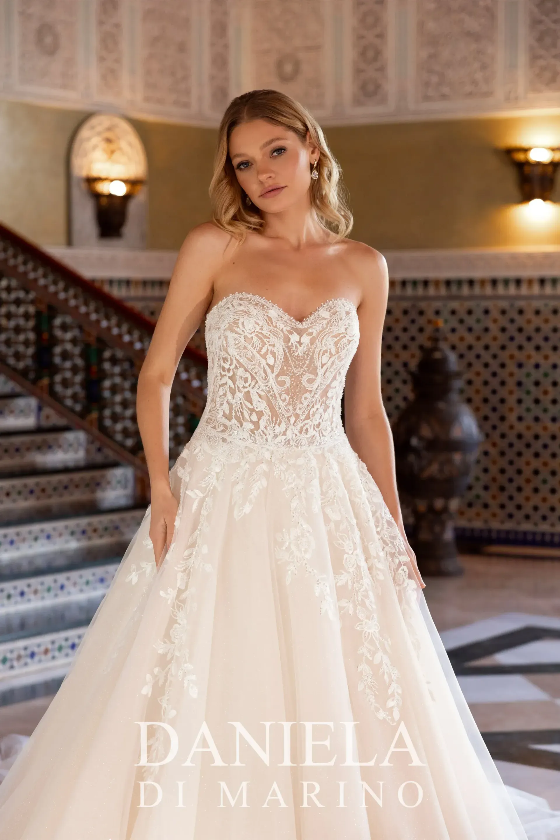 Woman in a white halter-neck wedding dress poses outdoors. She smiles, with her hands in the pockets of the full skirt.