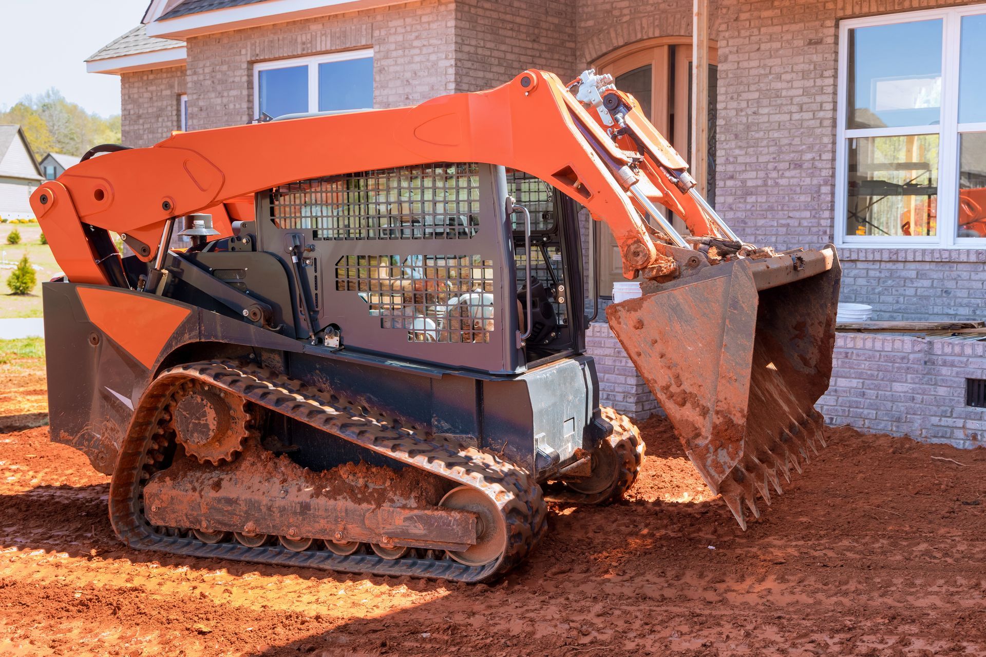 Orange Track Skid Steer With a Bucket Scooping Up Red Dirt — Dachboe Your Handyman In Ayr, QLD
