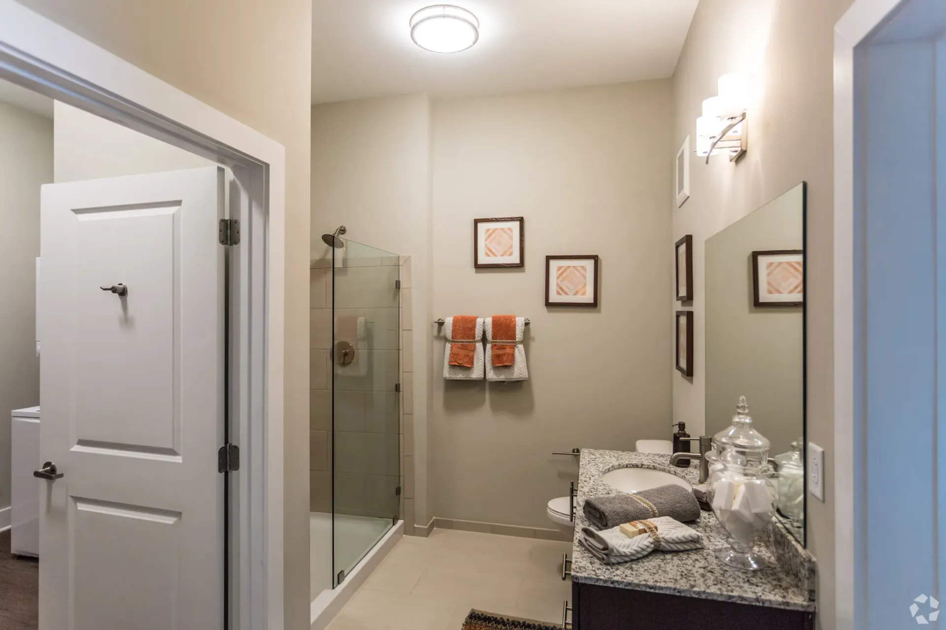 Modern apartment bathroom with glass shower, granite vanity, and towels on a rack.
