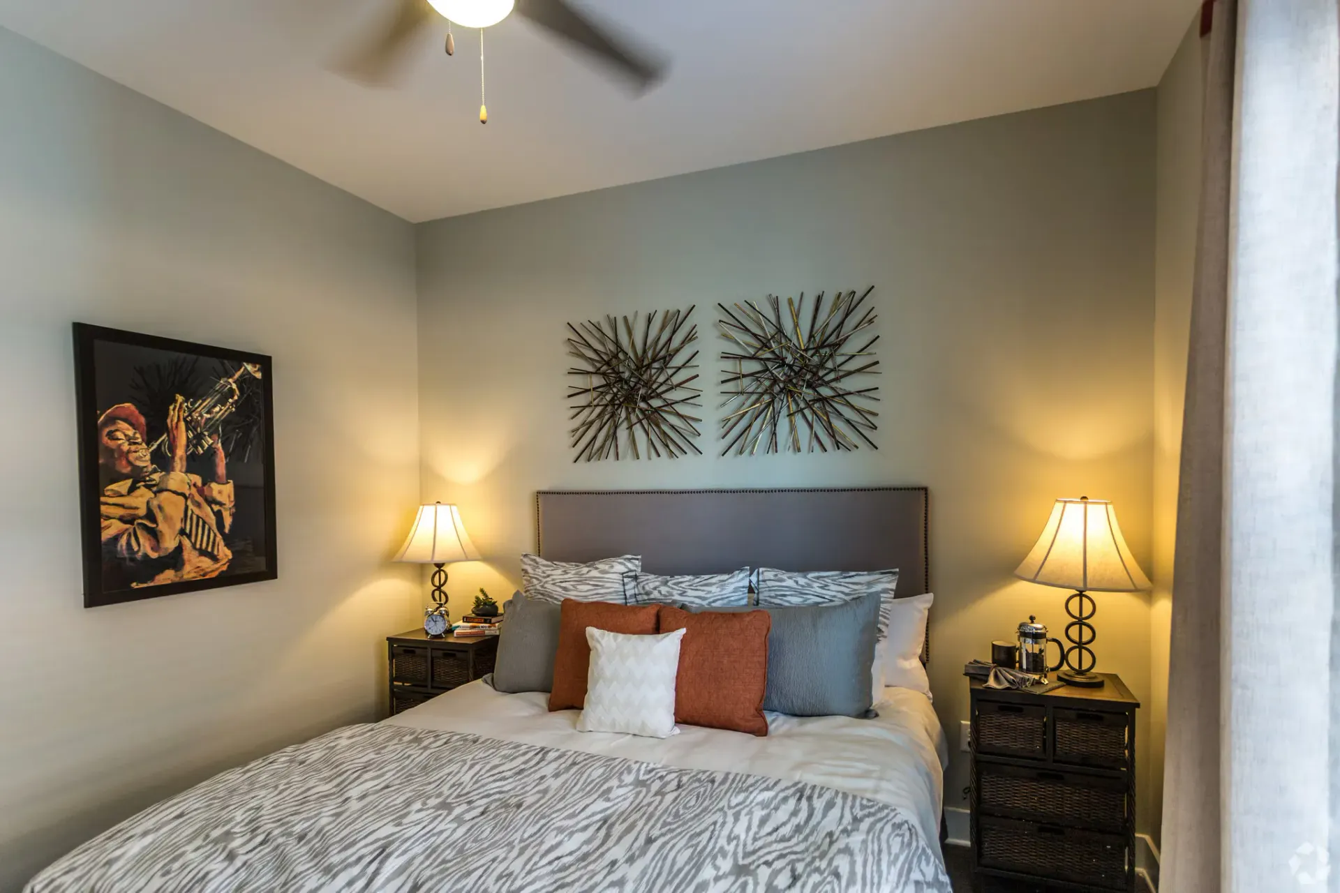 Bedroom with upholstered headboard, two nightstands with lamps, and two metal sunburst wall accents.