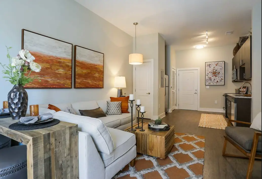 Living room and open kitchen of a modern apartment with a white sofa and wooden accents.