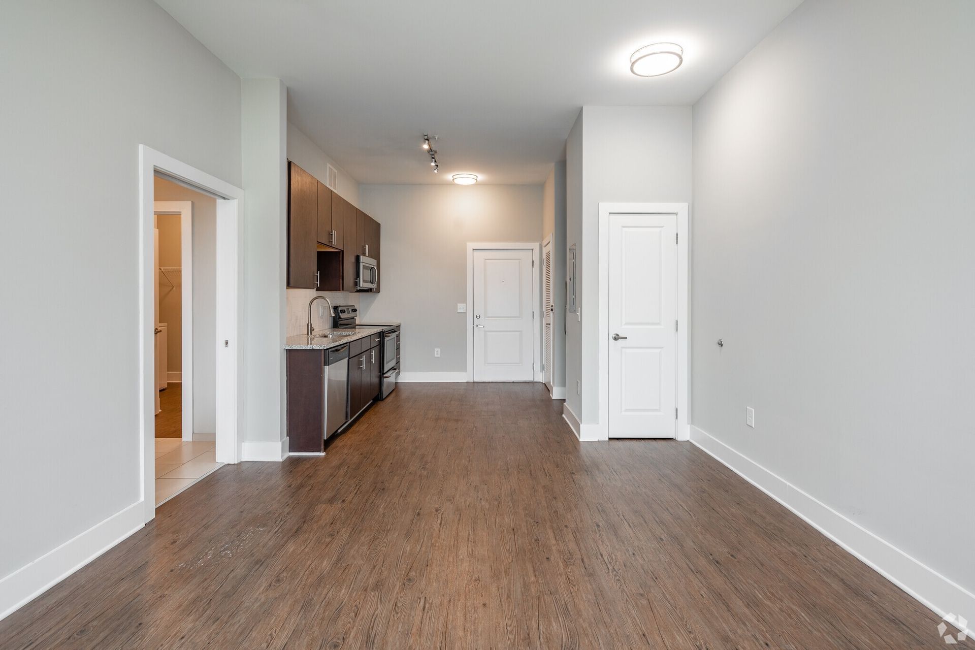 Open-concept apartment kitchen with stainless appliances and wood-look flooring.