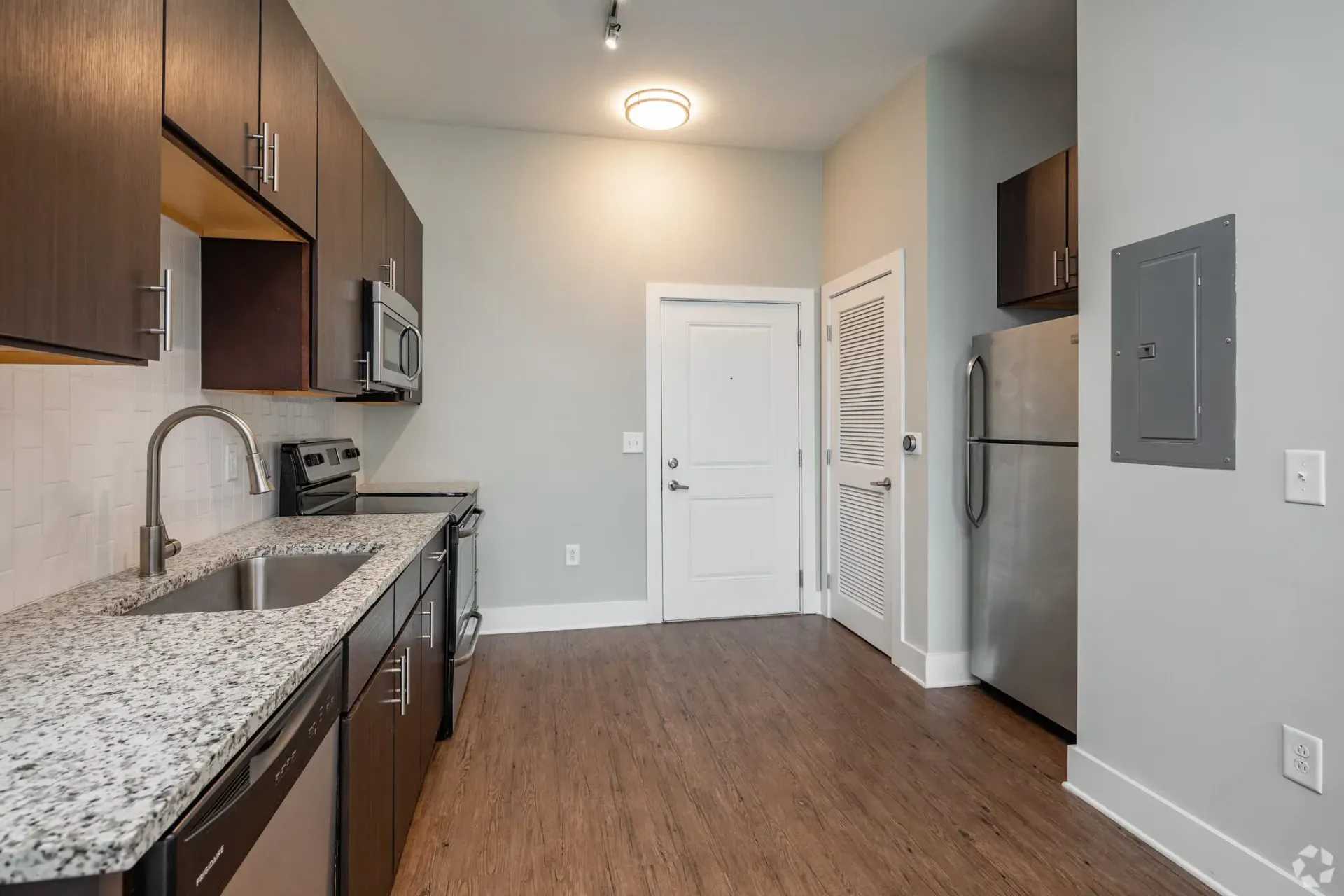 Modern apartment kitchen with dark wood cabinets, granite countertops, and stainless steel appliances.