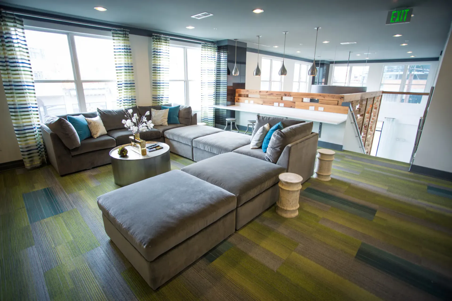 Spacious modern community lounge with a large gray sectional, coffee table, and striped curtains.