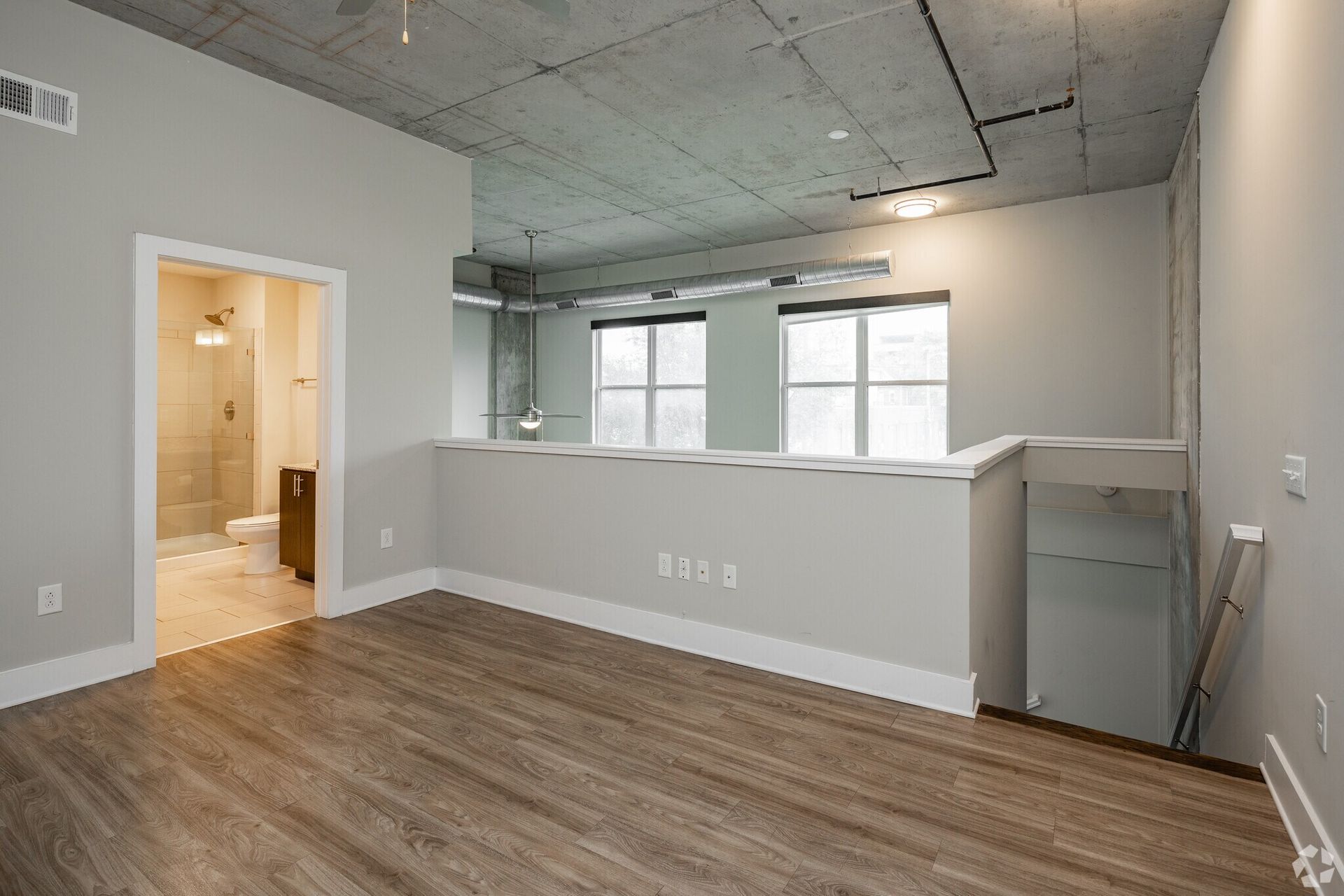 Loft-style living area with an exposed concrete ceiling, half-wall railing, and a doorway to a bathroom.