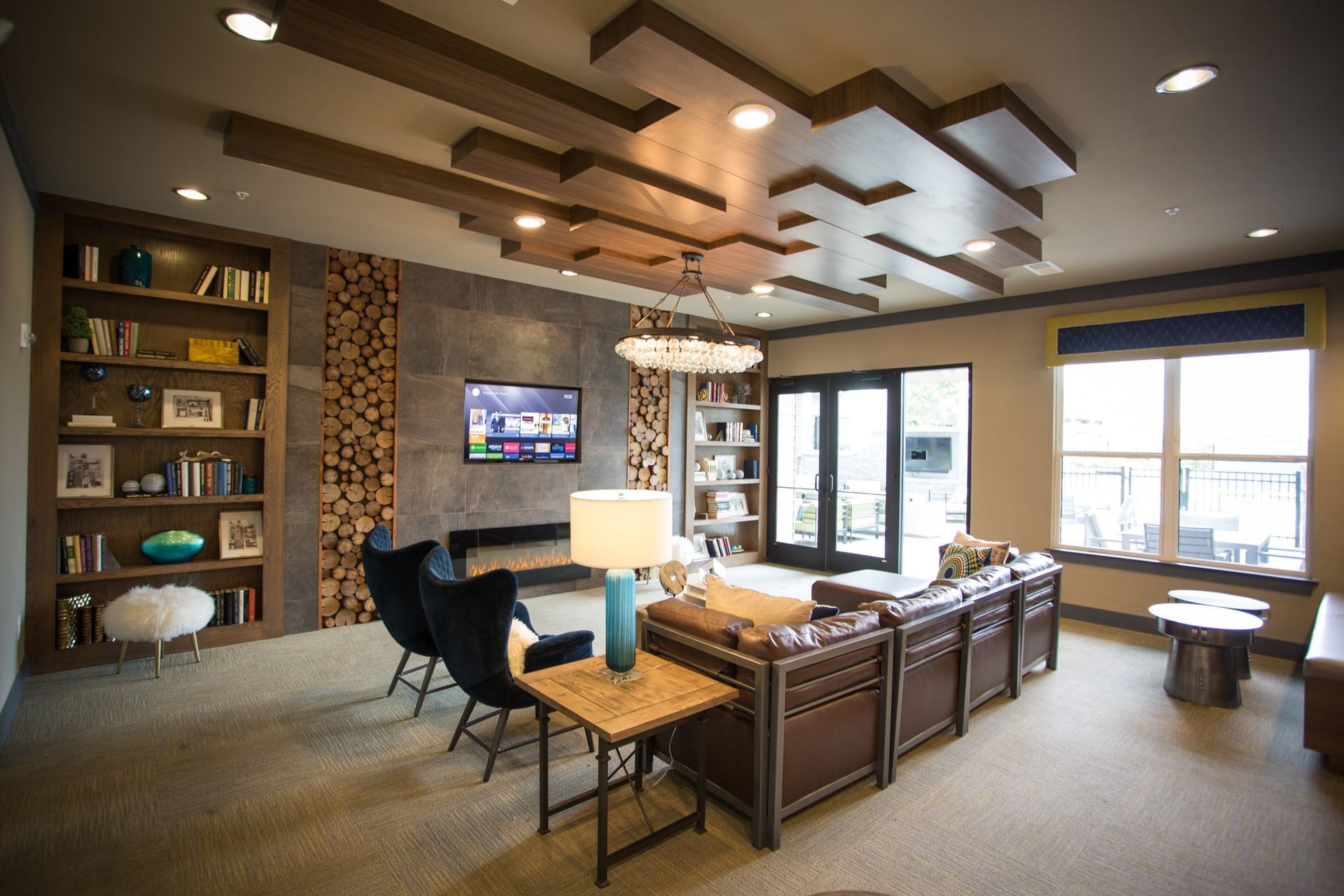 Indoor apartment community lounge with brown leather sofas, chairs, bookshelves, a fireplace, and a TV.