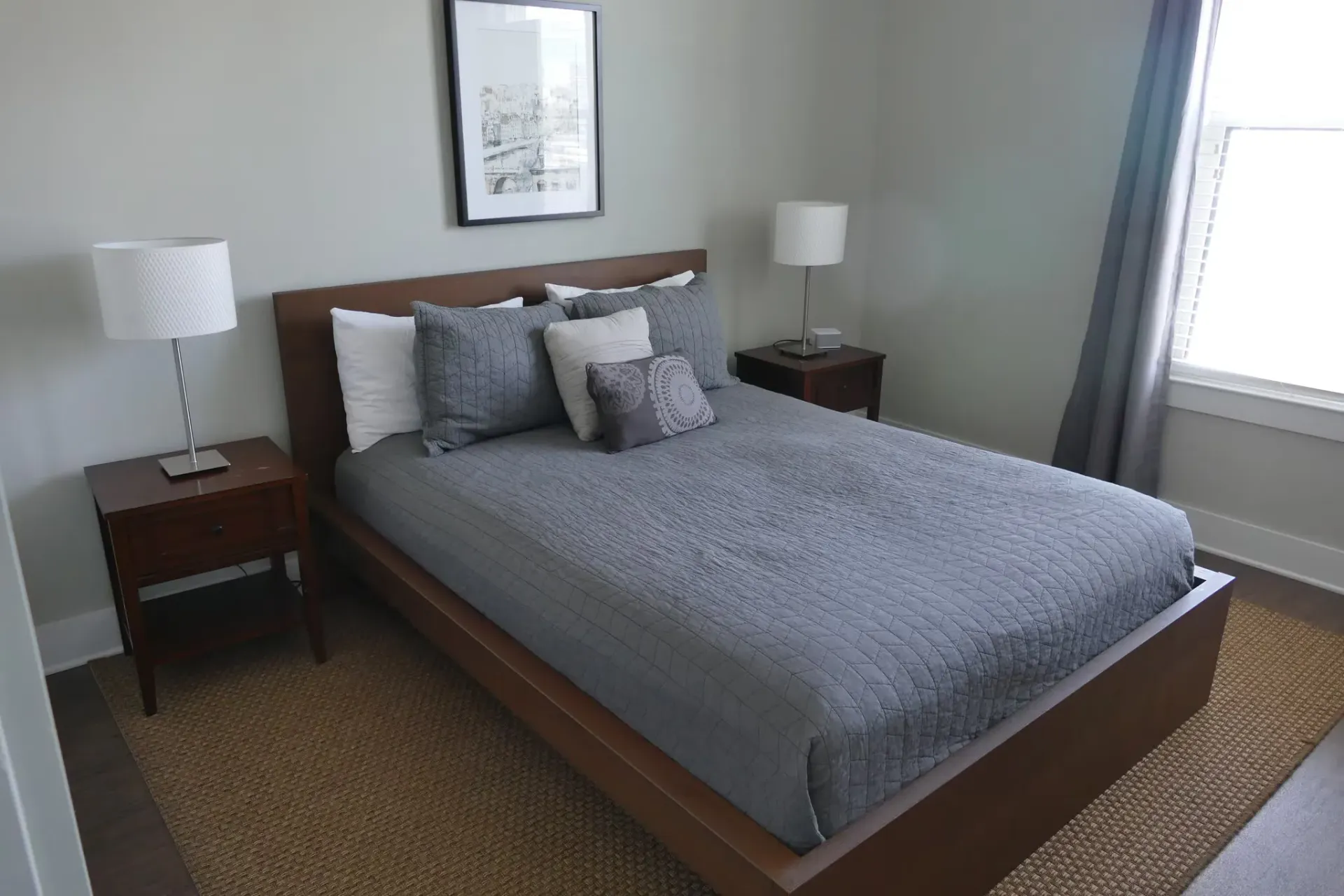 Bedroom with a wooden platform bed, gray quilt bedding, two nightstands, and a window with curtains.
