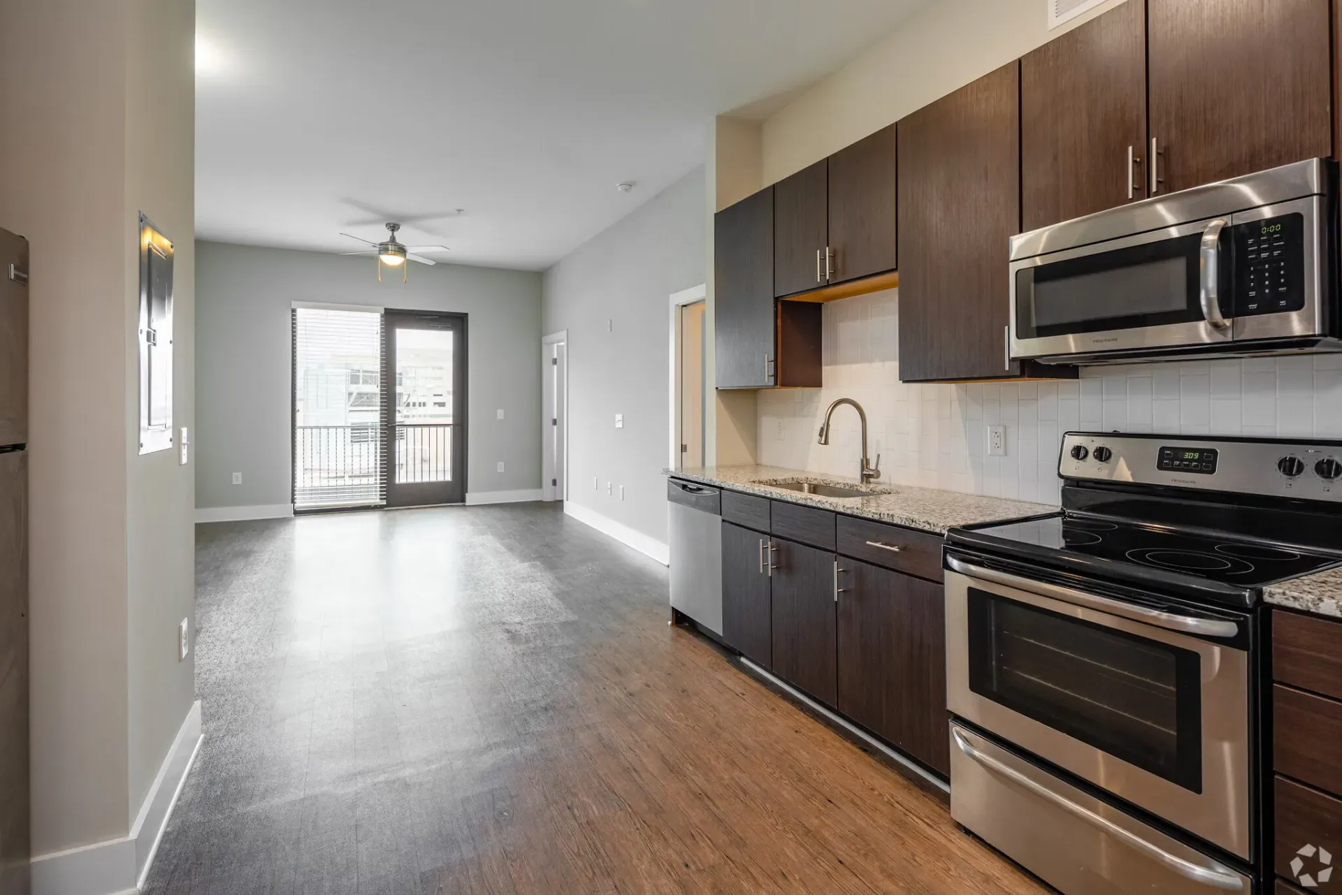 Open-concept kitchen with dark maple cabinets, stainless steel appliances, and a balcony door.