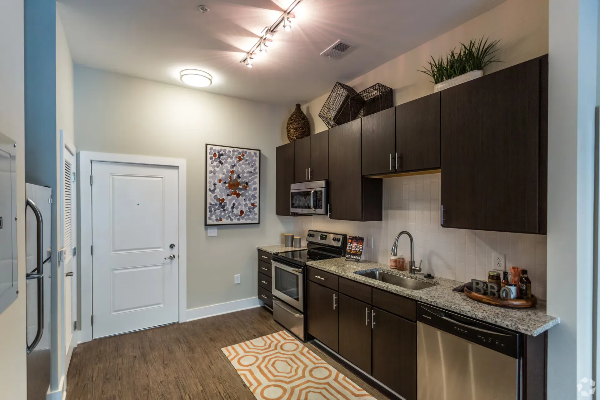Modern apartment kitchen with dark wood cabinets, stainless steel appliances, and granite countertops.