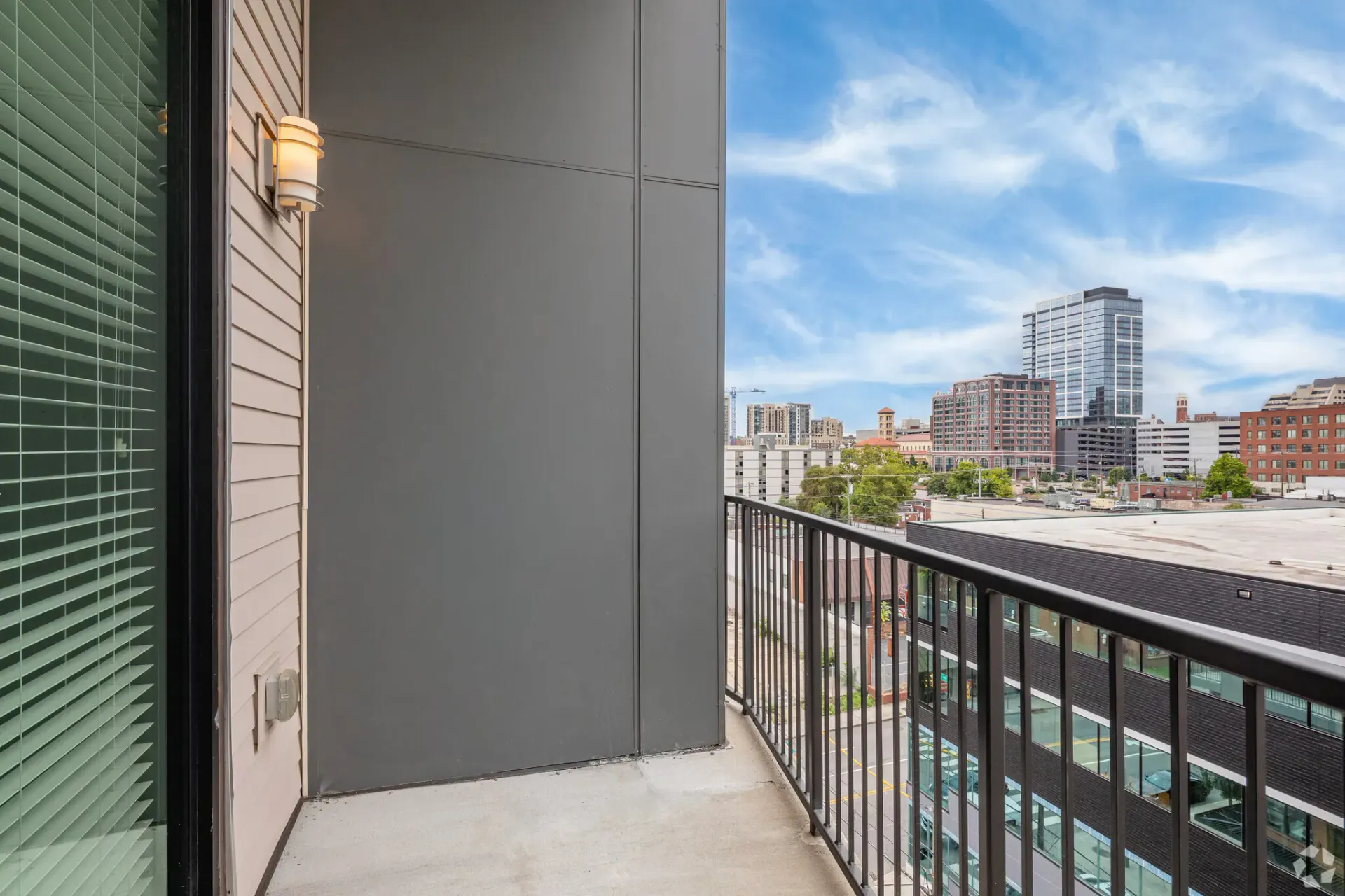 Balcony of an apartment with a sliding glass door, railing, and a downtown skyline.