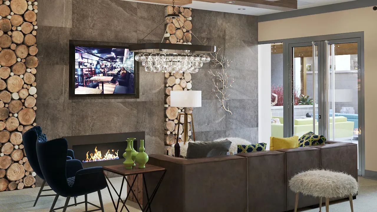 Modern community lounge with a fireplace, stone walls, log accents, and glass doors opening to an outdoor patio.