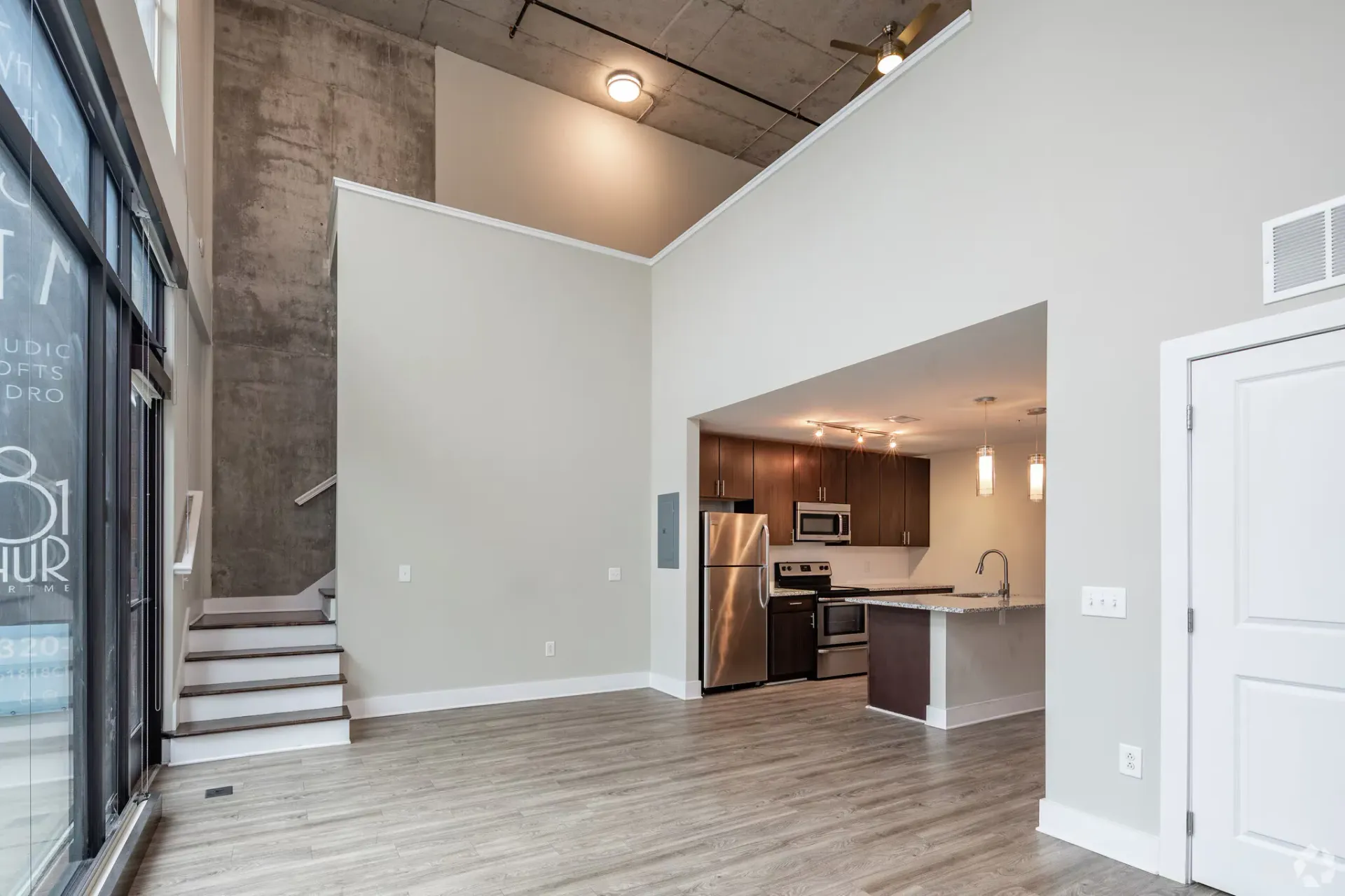 Open-concept living area with a modern kitchen, stainless-steel appliances, and a staircase.