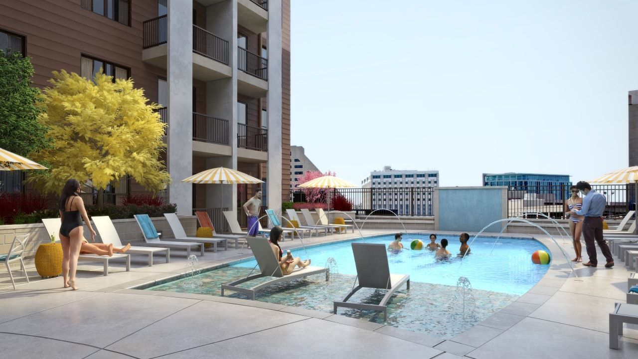 Outdoor rooftop pool area at an apartment complex with lounge chairs, umbrellas, and people swimming.