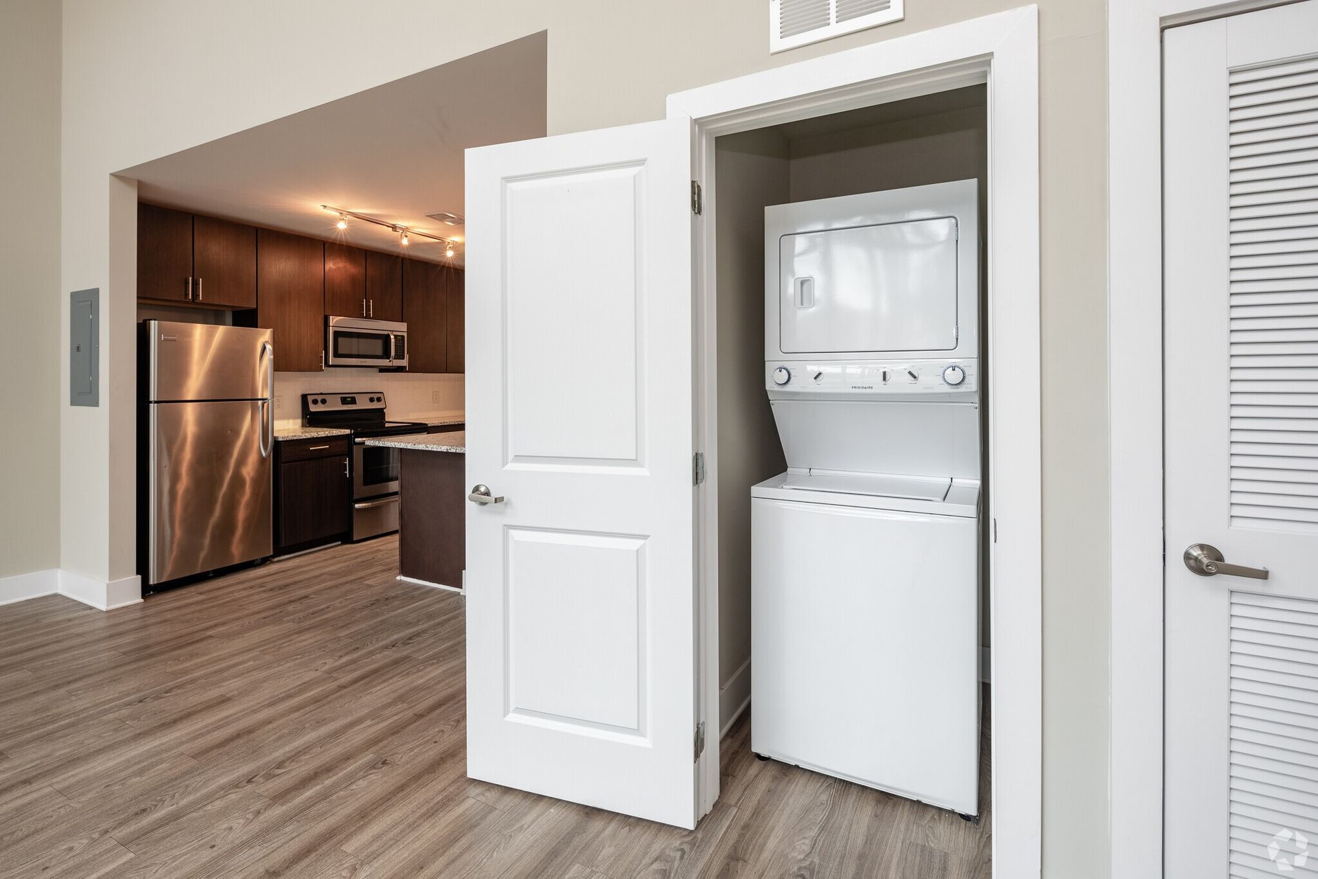 Open doorway to a modern kitchen with stainless appliances and a stacked washer/dryer in a closet.