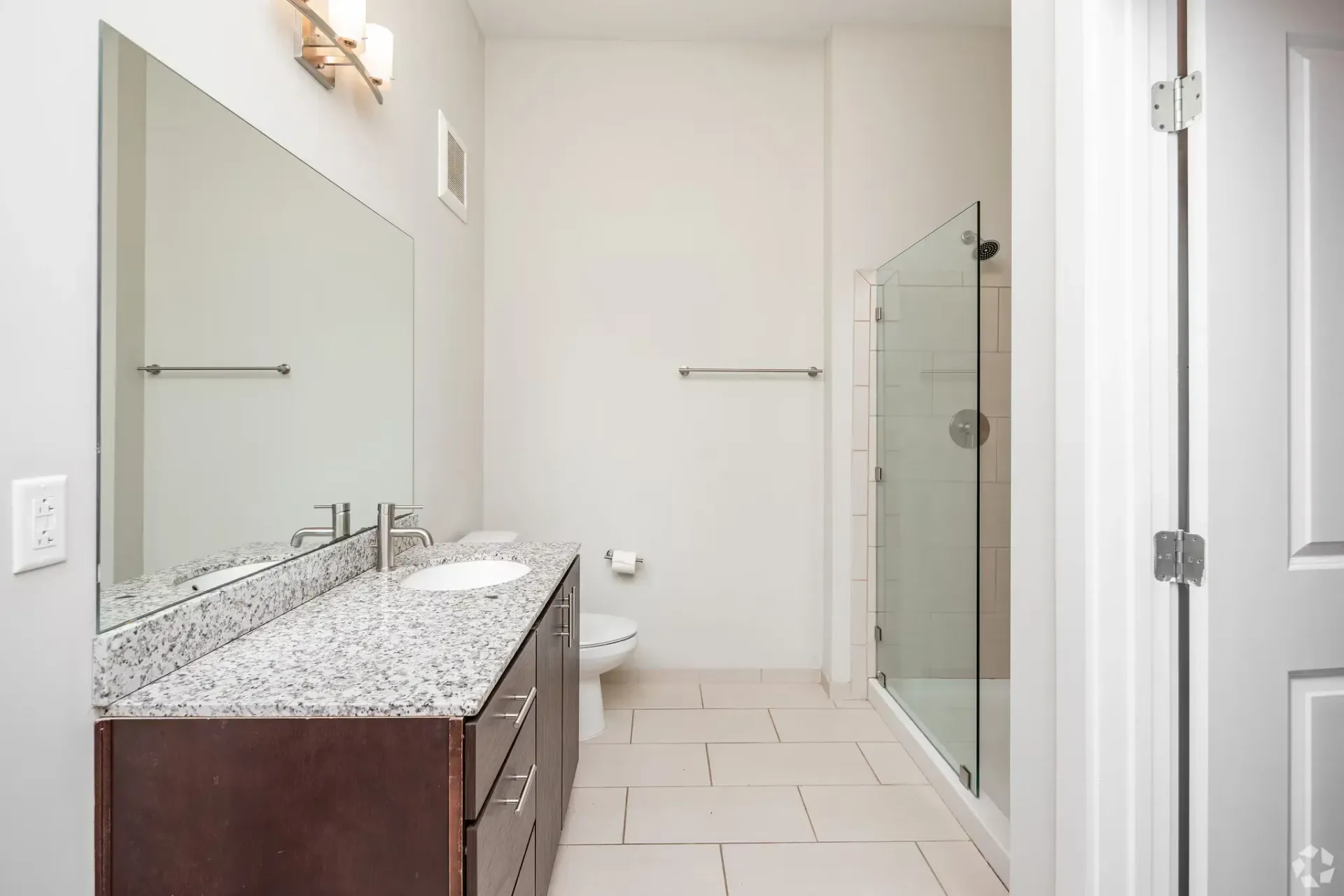 Bathroom with granite vanity, single sink, mirror, toilet, and glass-enclosed shower.
