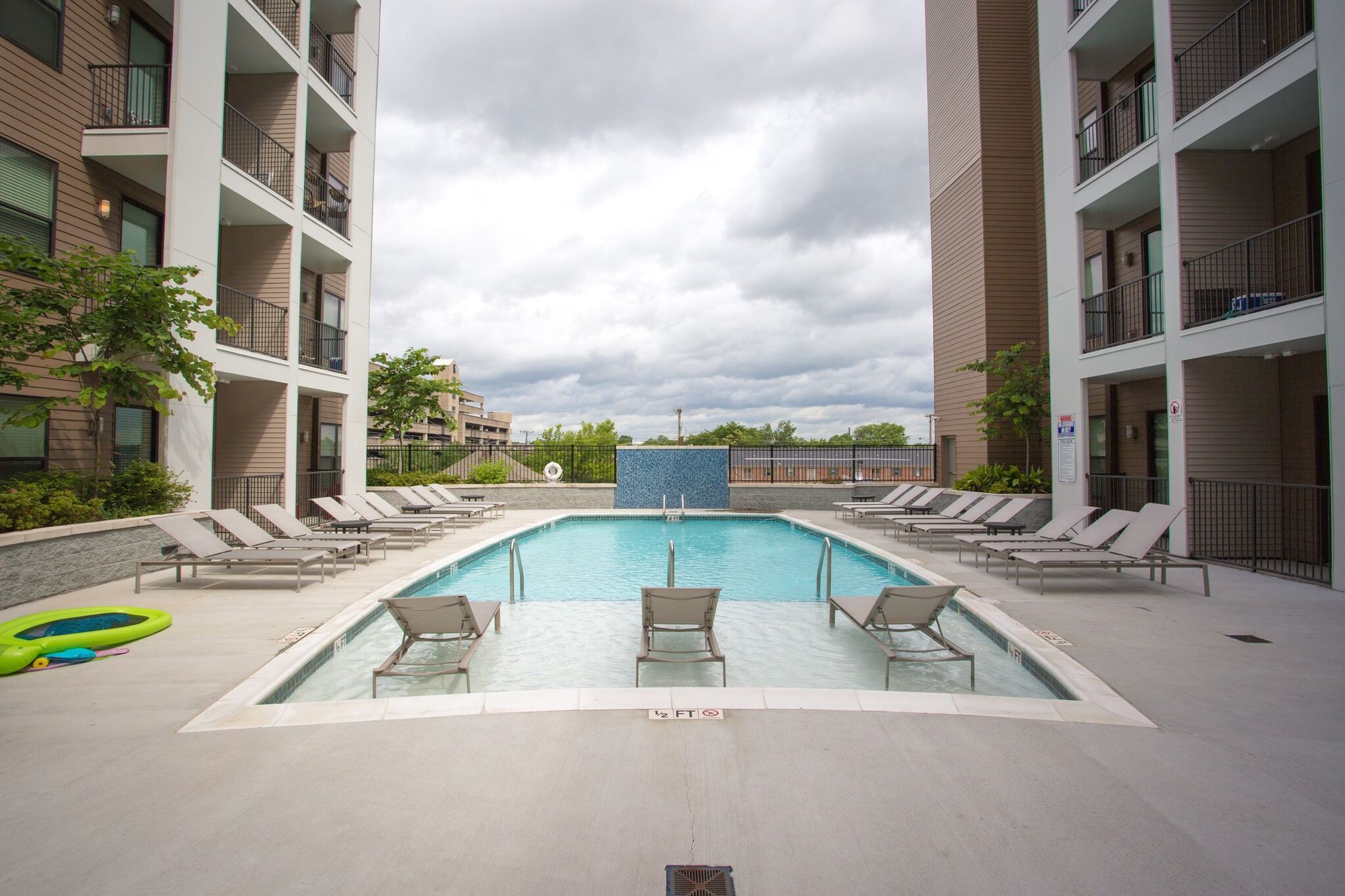 Outdoor community pool surrounded by lounge chairs between modern apartment buildings.