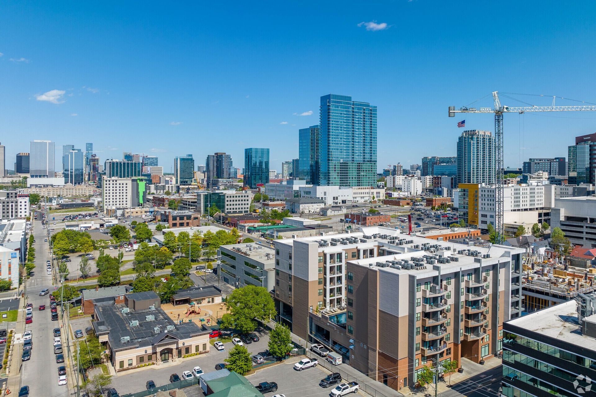 Aerial view of a city skyline featuring modern apartment buildings and a construction crane against a clear blue sky.
