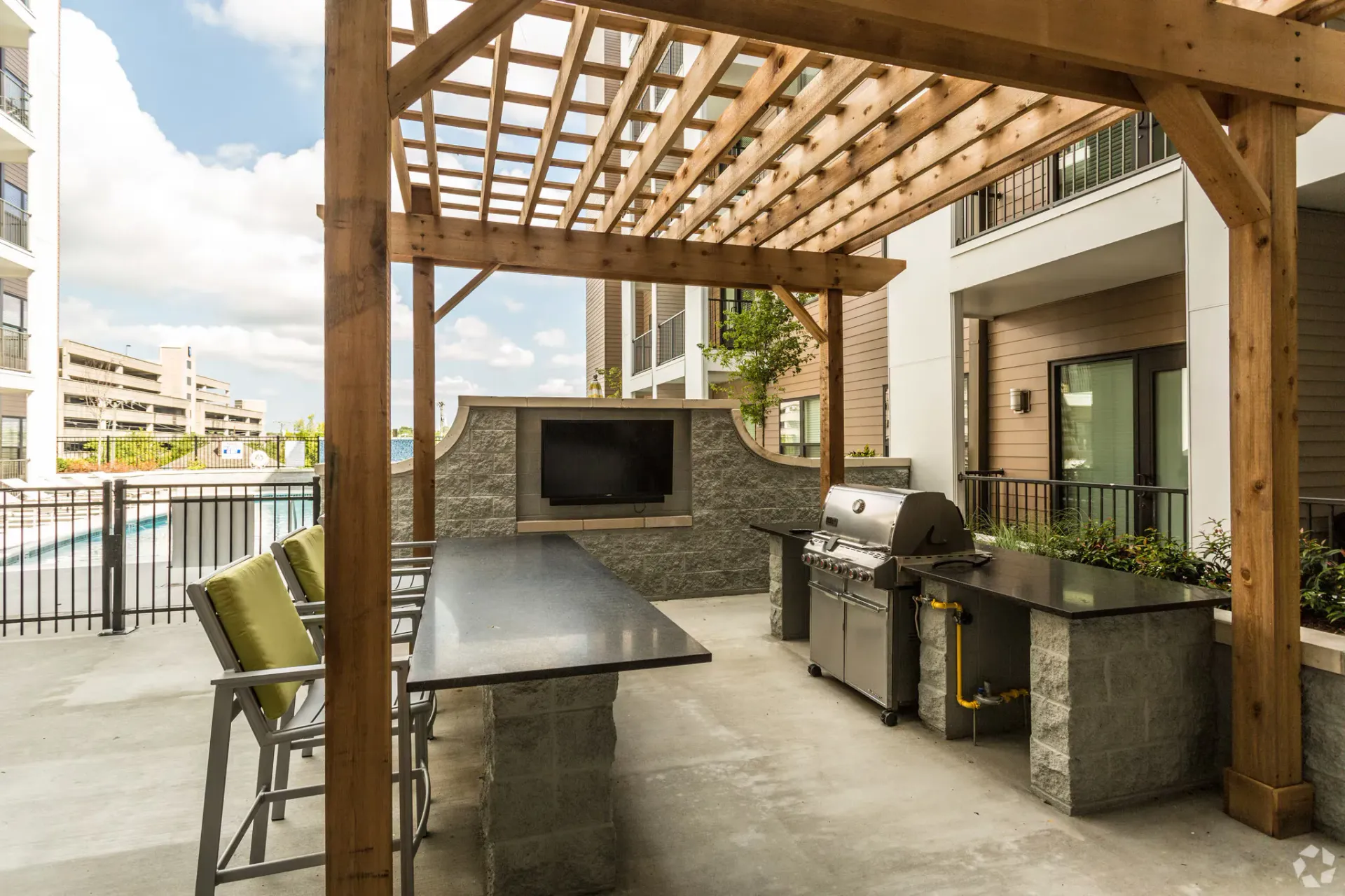 Outdoor community grilling area under a wooden pergola with a built-in grill and TV.