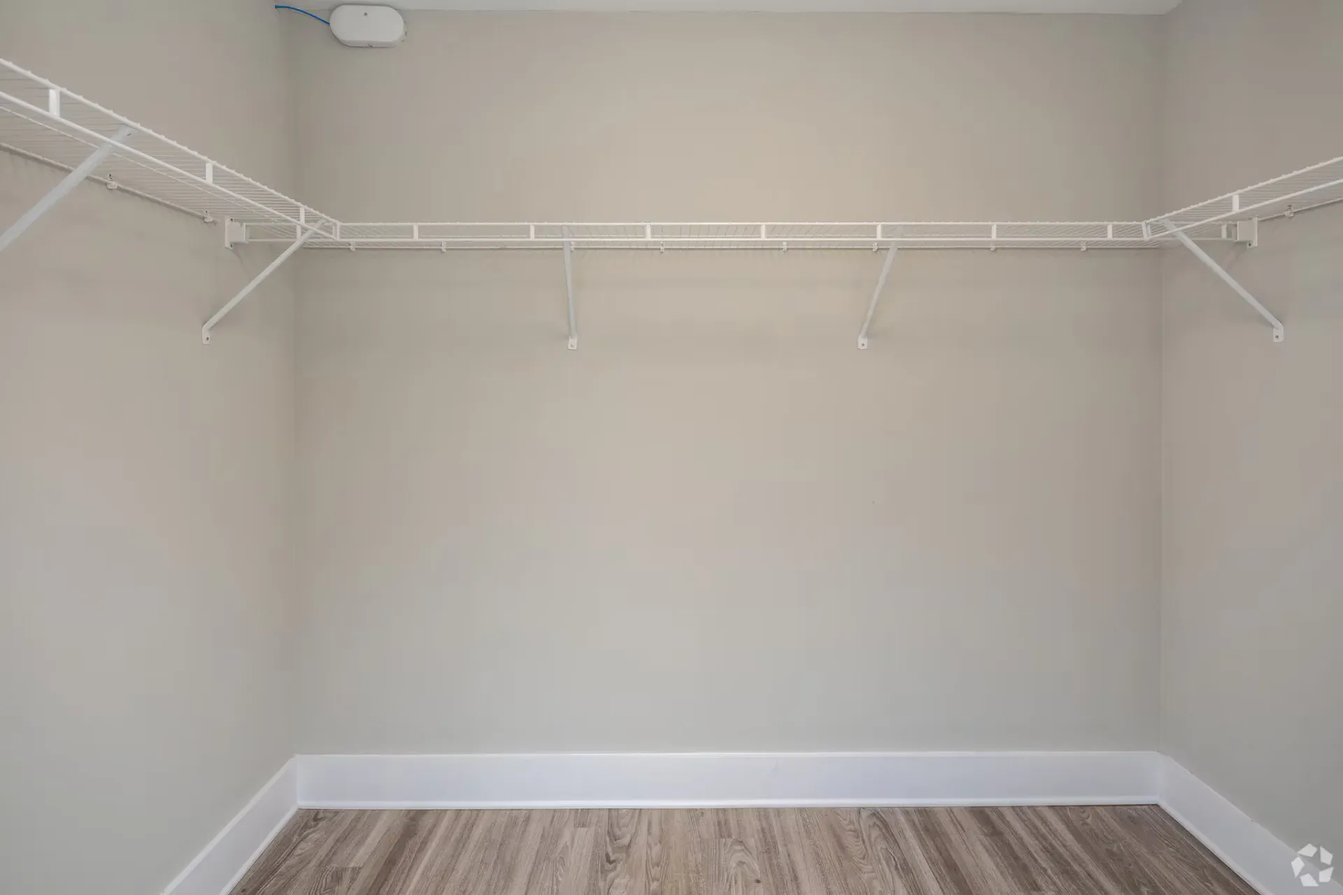 Empty walk-in closet with white wire shelving and light wood flooring.